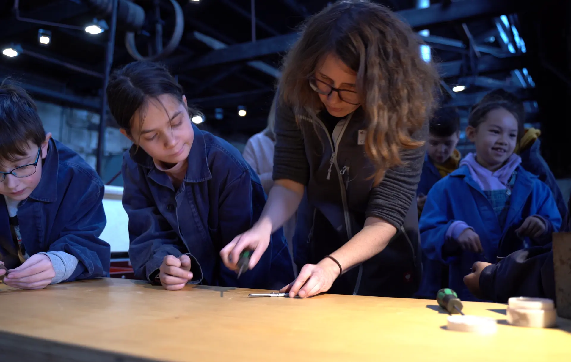 Eine Museumspädagogin führt mit einigen Kindern ein museumspädagogisches Programm an einem Tisch durch.