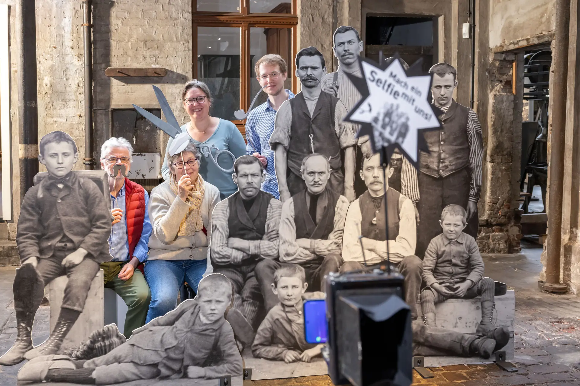 Eine Gruppe macht ein Foto an der Selfie-Station, die aus Aufstellern von der historischen Belegschaft besteht.