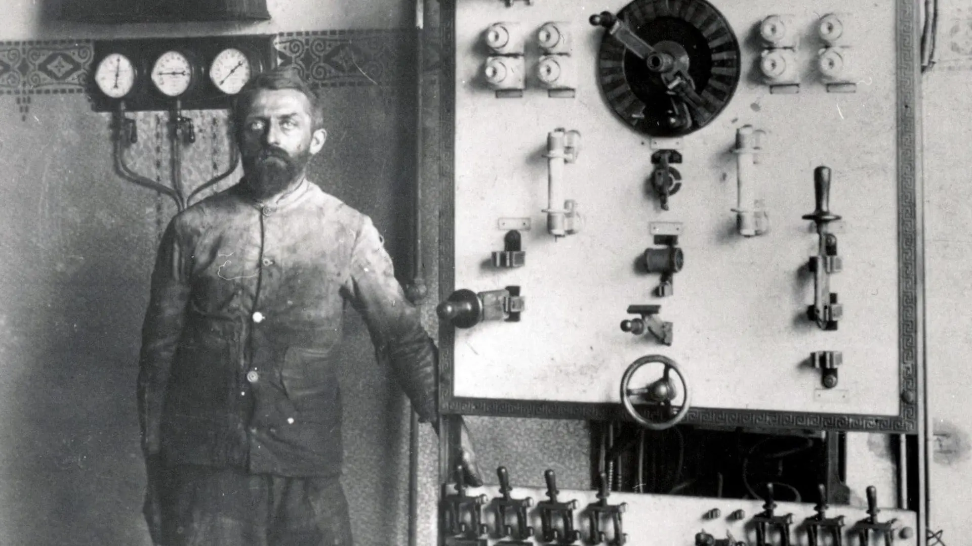 Historisches schwarz-weiß Foto eines Arbeiters neben einer Schalttafel.