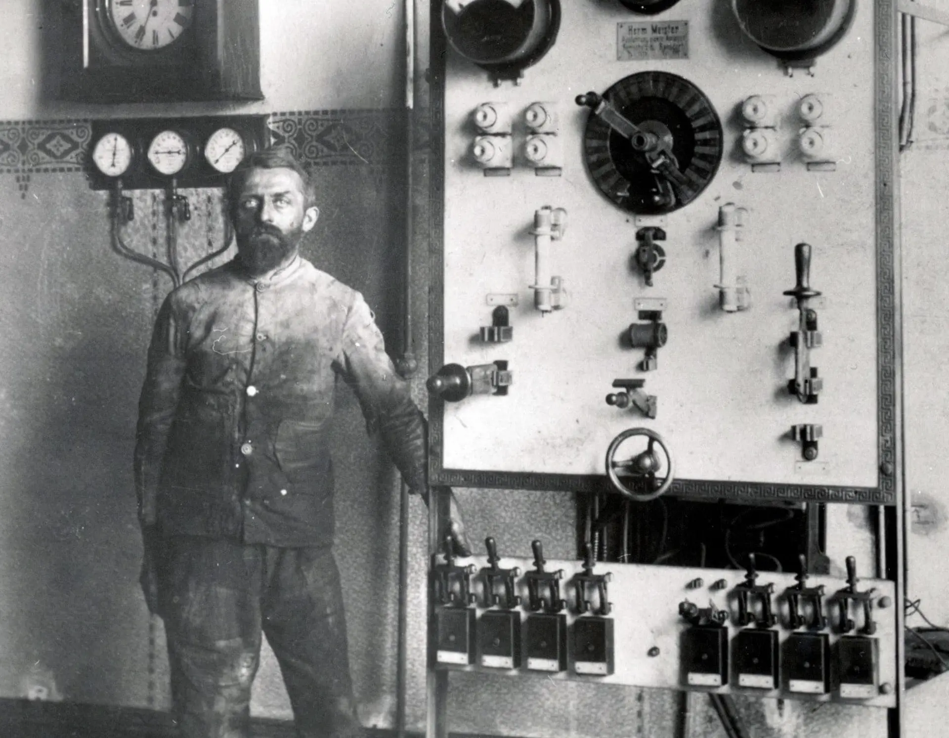 Historisches schwarz-weiß Foto eines Arbeiters neben einer Schalttafel.