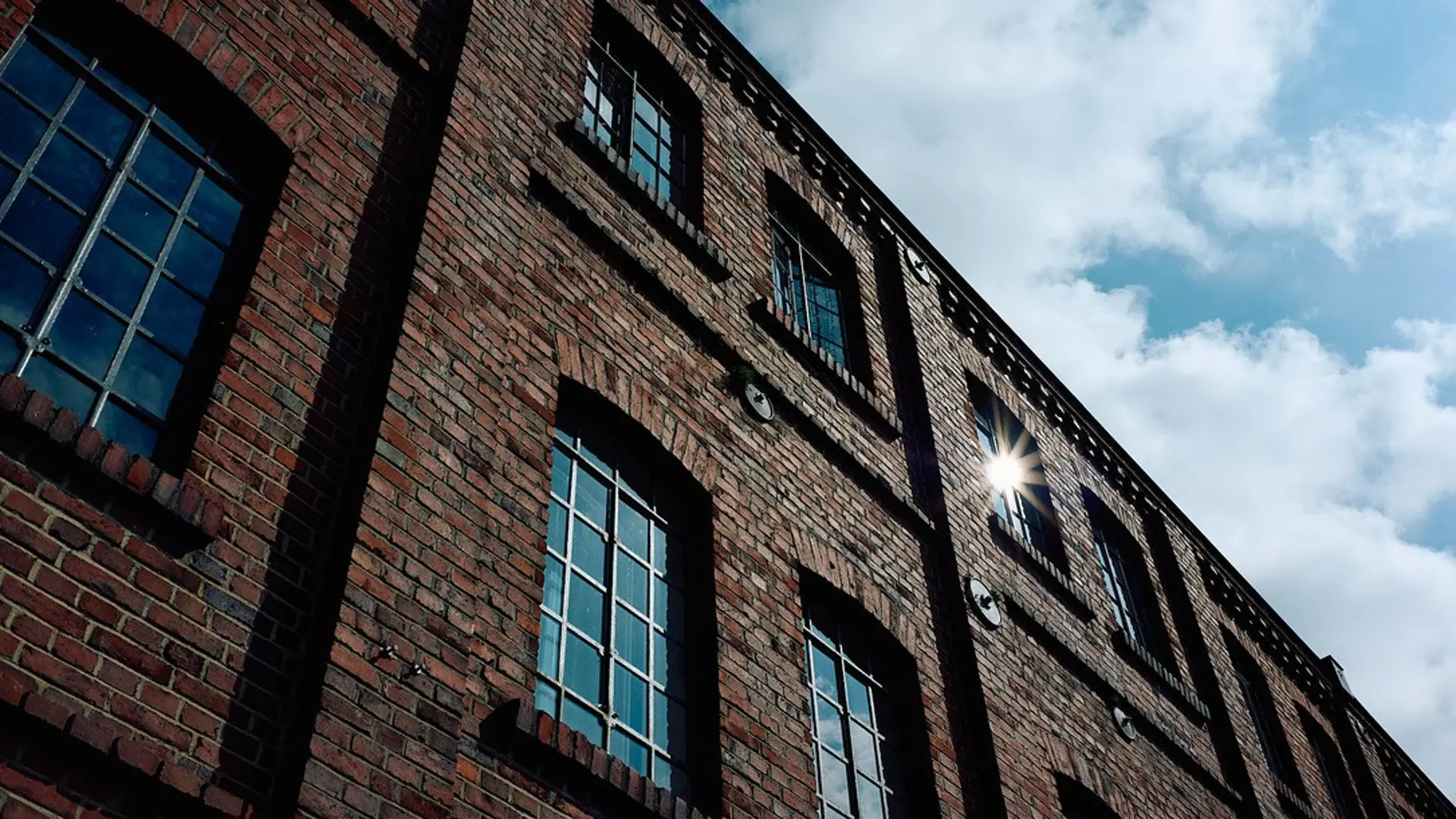 Ein Backsteingebäude von schräg unten vor blauem Himmel. Die Fenster reflektieren die Sonne.