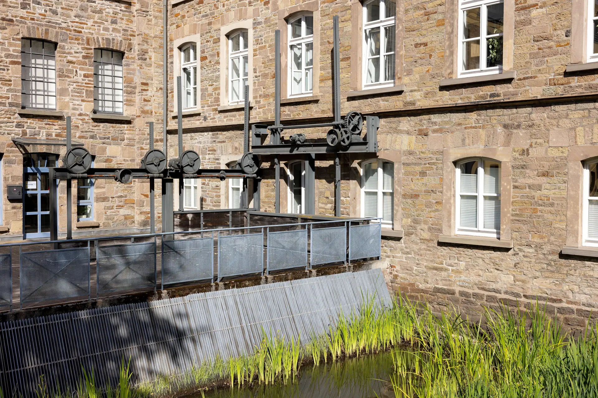 Gewässer vor einem Gebäude aus Stein, in dem sich Schütze aus Metall befinden.