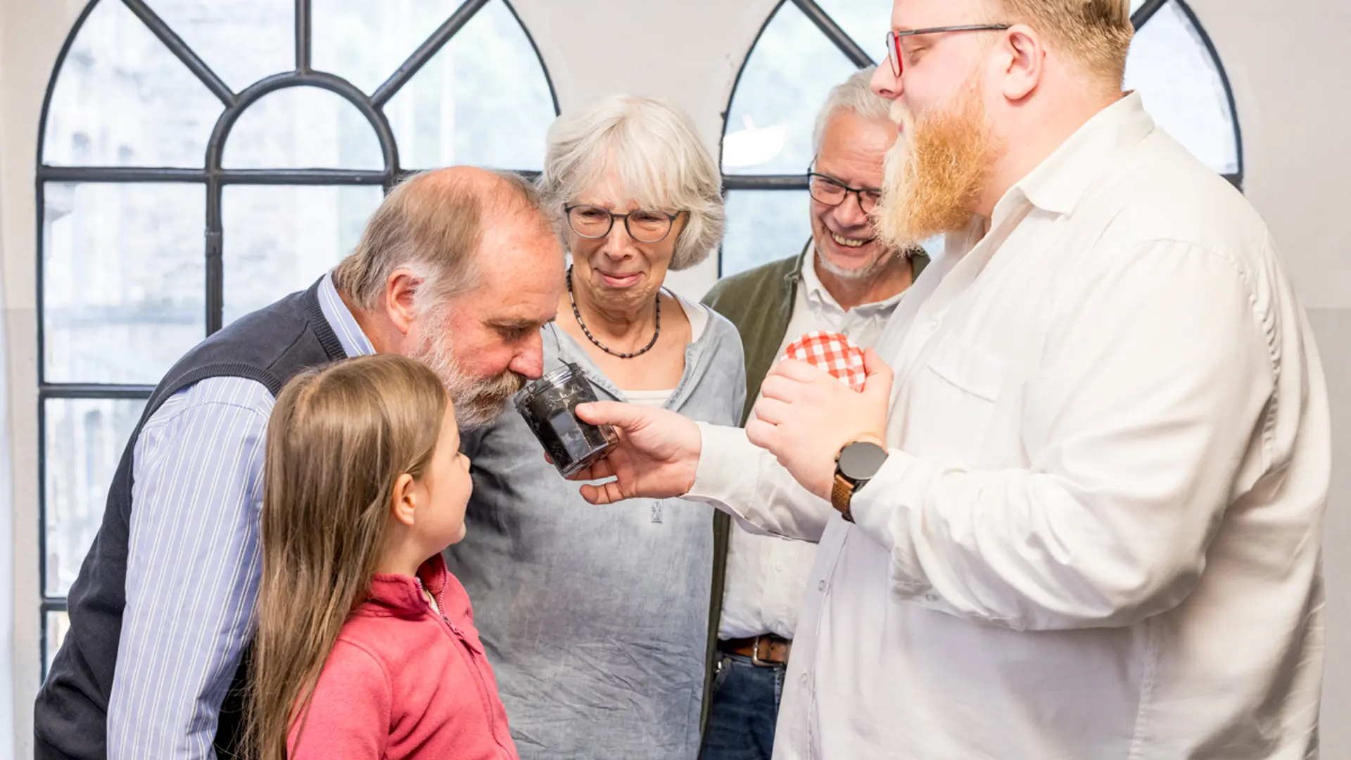 Drei Erwachsene und ein Mädchen machen eine Sinnesführung. Der Gästeführung hält ein Glas in der Hand, an dem ein Mann riecht.