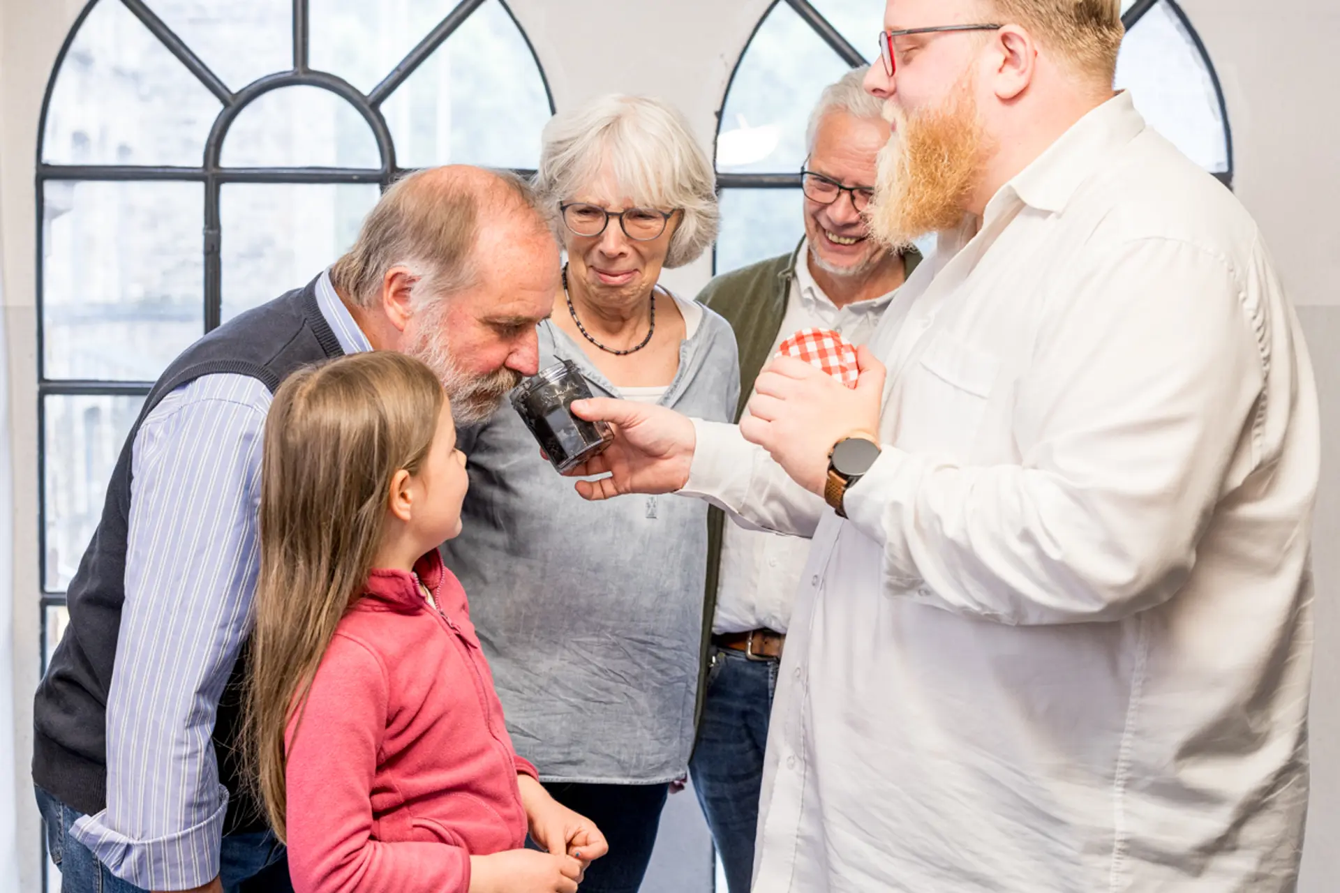 Drei Erwachsene und ein Mädchen machen eine Sinnesführung. Der Gästeführung hält ein Glas in der Hand, an dem ein Mann riecht.