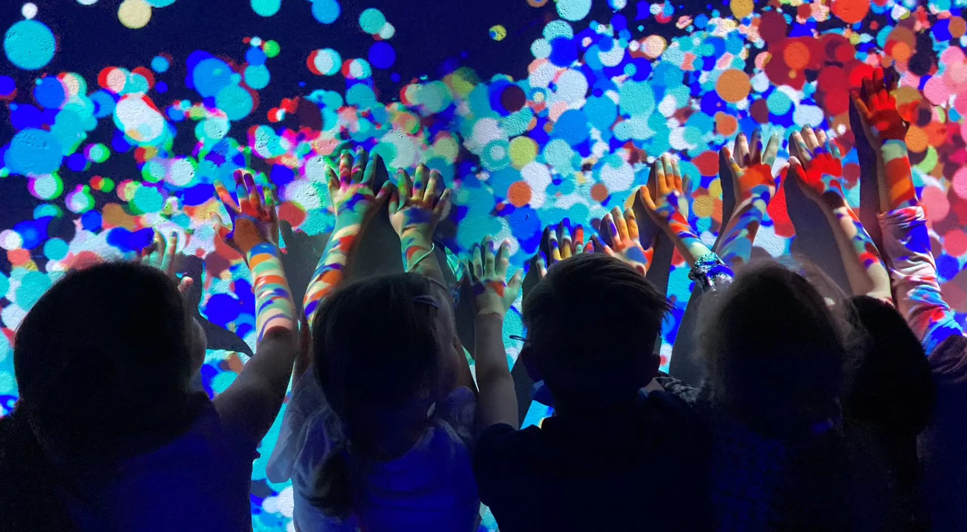 Mehrere Kinder fassen mit den Händen an eine bunt beleuchtete Wand.