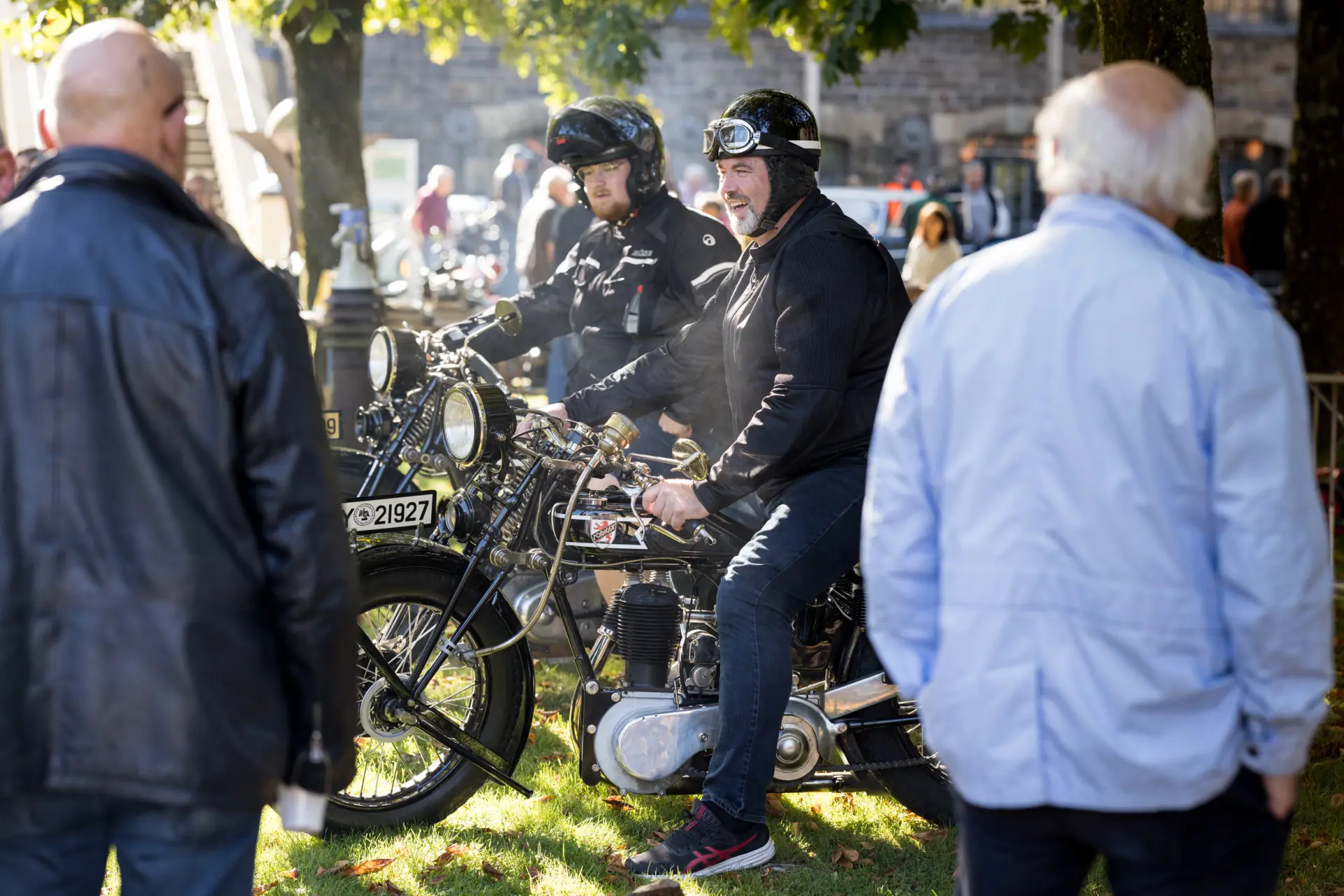 Einige Männer auf Motorrädern, die von zwei anderen Männern betrachtet werden.