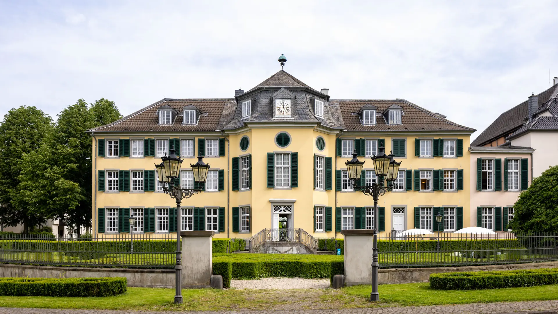 Ein gelbes barockes Herrenhaus mit grünen Fensterläden.