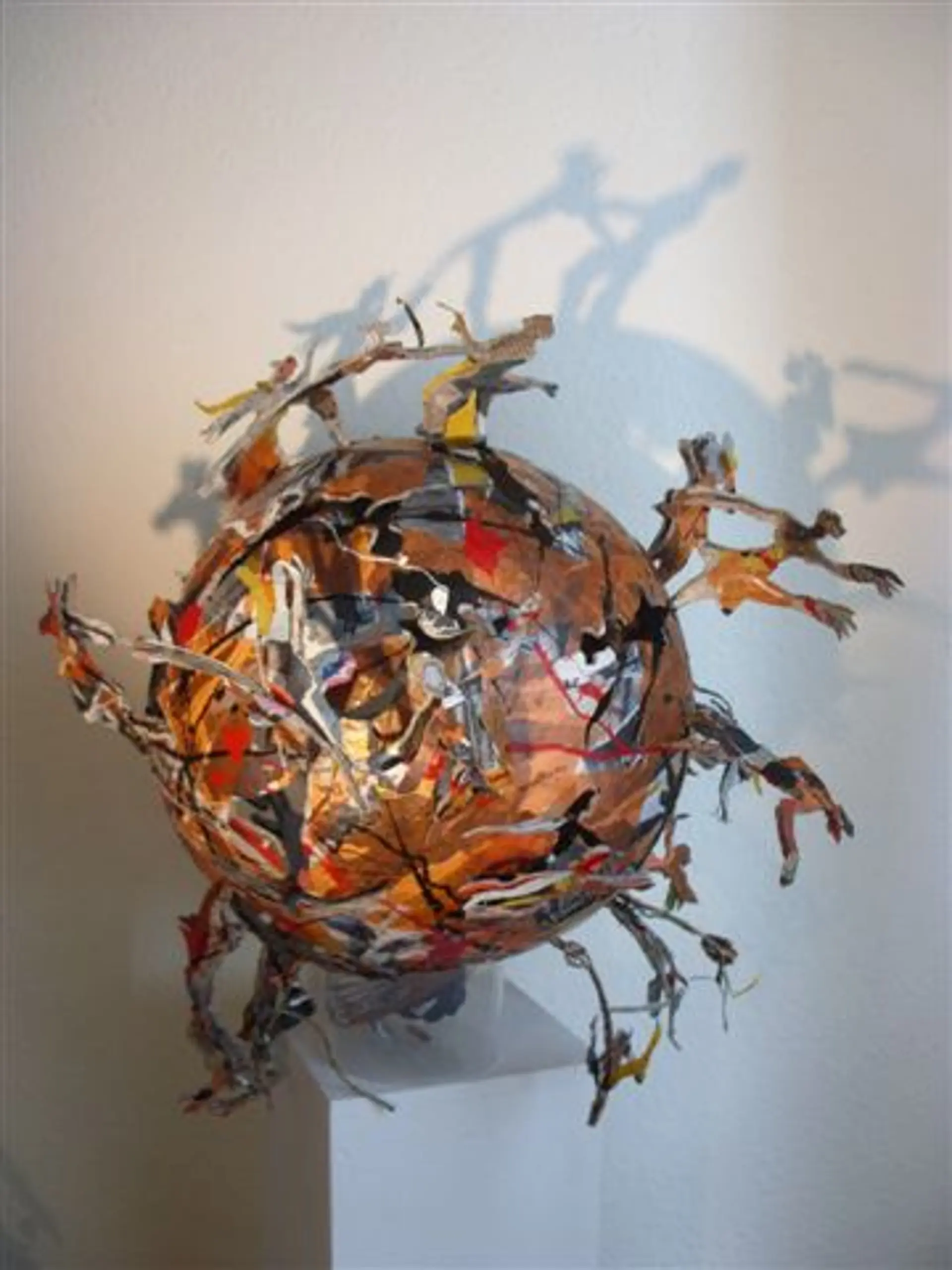 Skulptur aus Papierstreifen in Form einer Kugel. Auf der Kugel stehen verschiedene Figuren, die auch aus Papier sind. 
