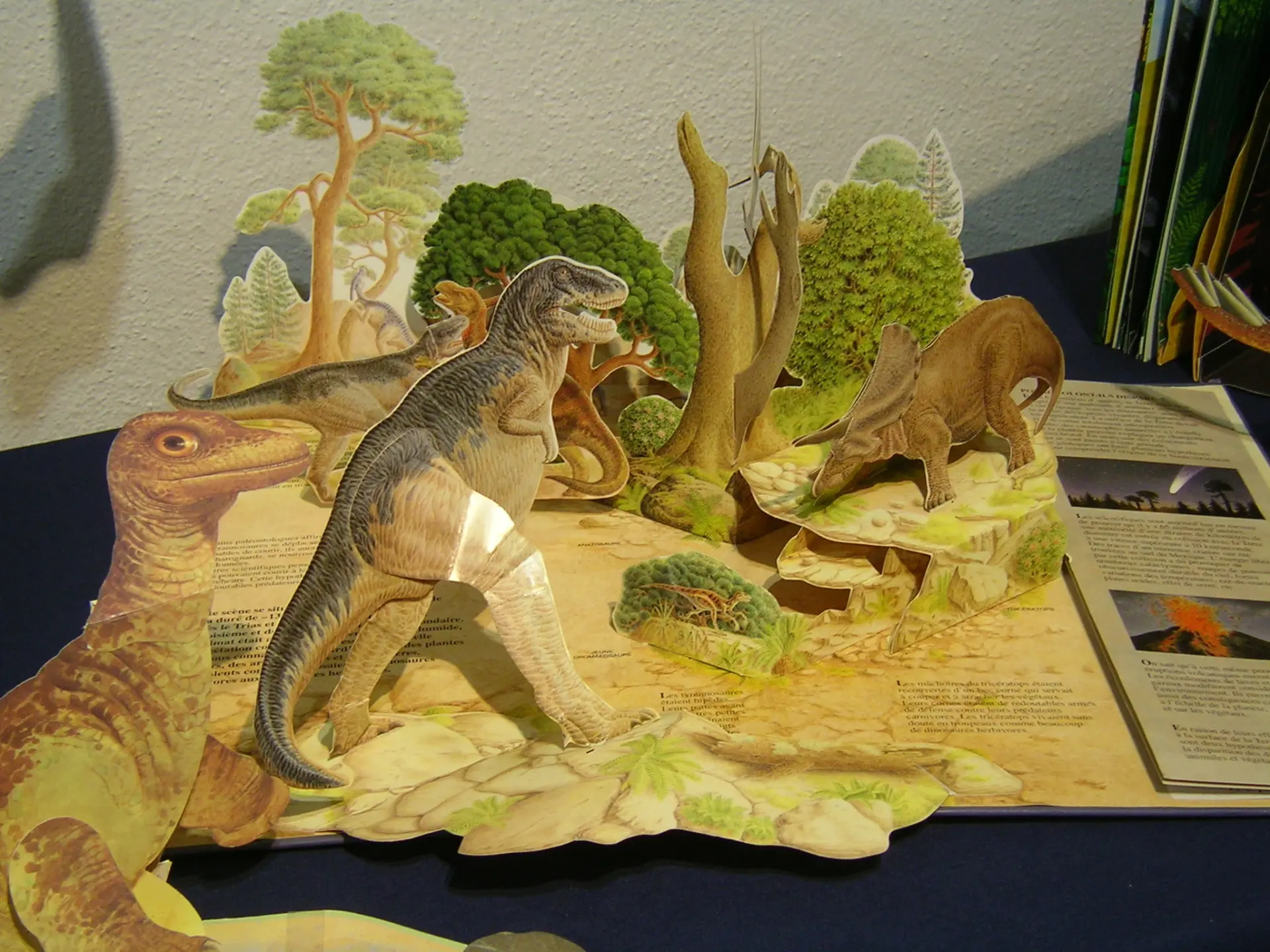 Ein offenes Buch, aus dem verschiedene Papierfiguren herausragen. Einige Figuren sehen aus wie Bäume. Die anderen Figuren stellen verschiedene Dinosaurier dar. 