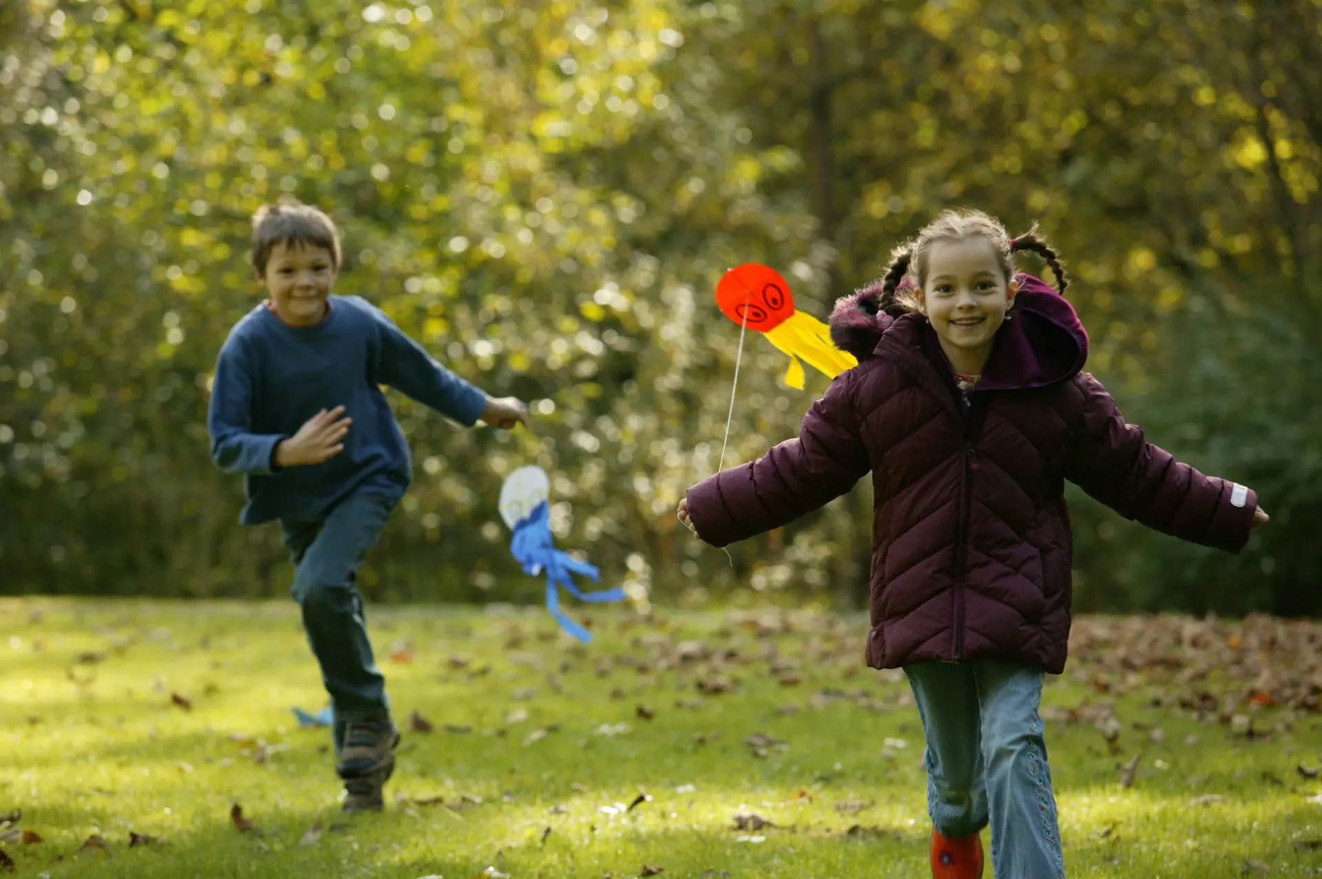 Zwei Kinder rennen mit Papierdrachen in der Hand über eine Wiese.