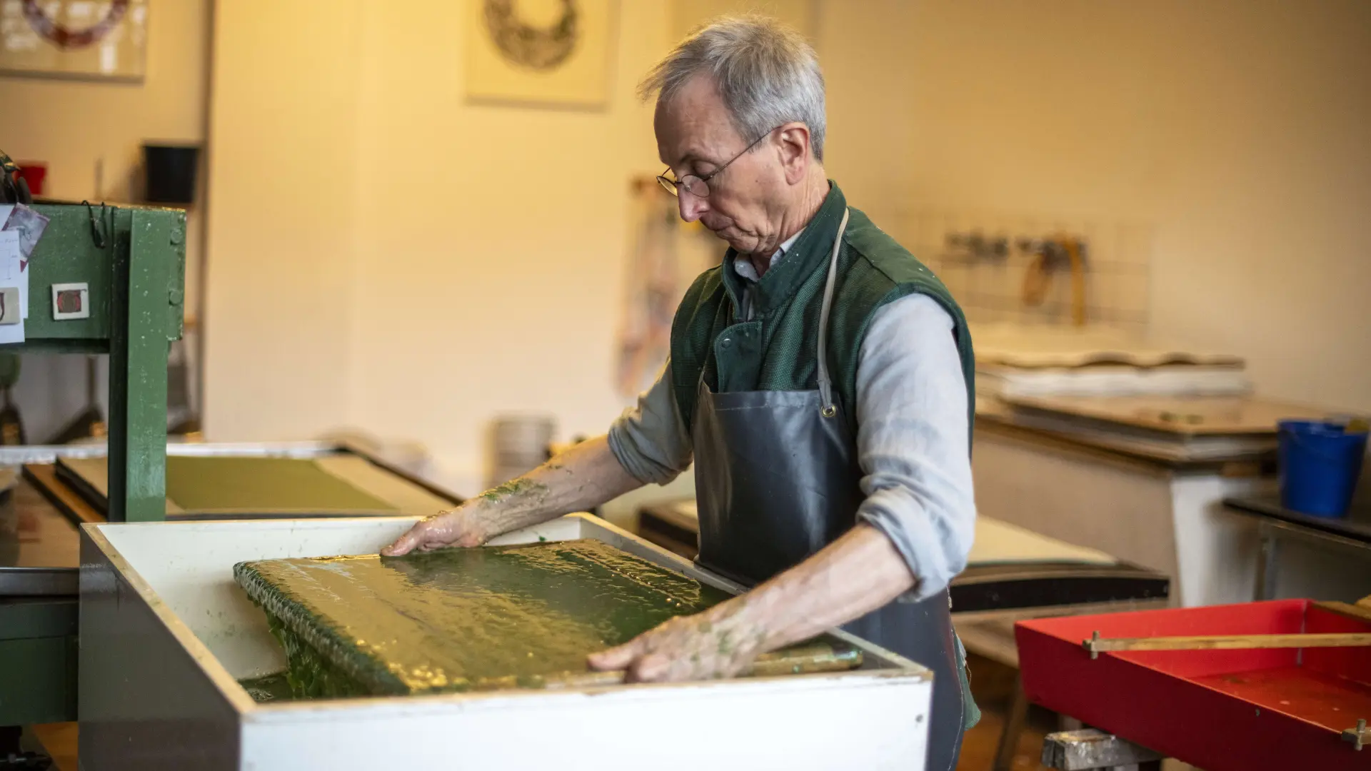 Ein Mann beim Papierschöpfen in seinem Atelier – hier wird aus Fasern, Wasser und Papierbrei ein einzigartiger Papierbogen.