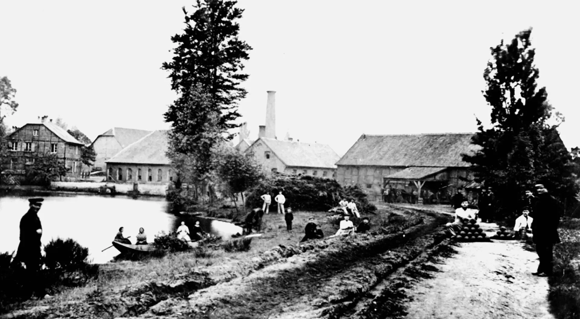 Historisches Schwarzweiß-Foto von Gebäuden, im Vordergrund Menschen und ein Teich