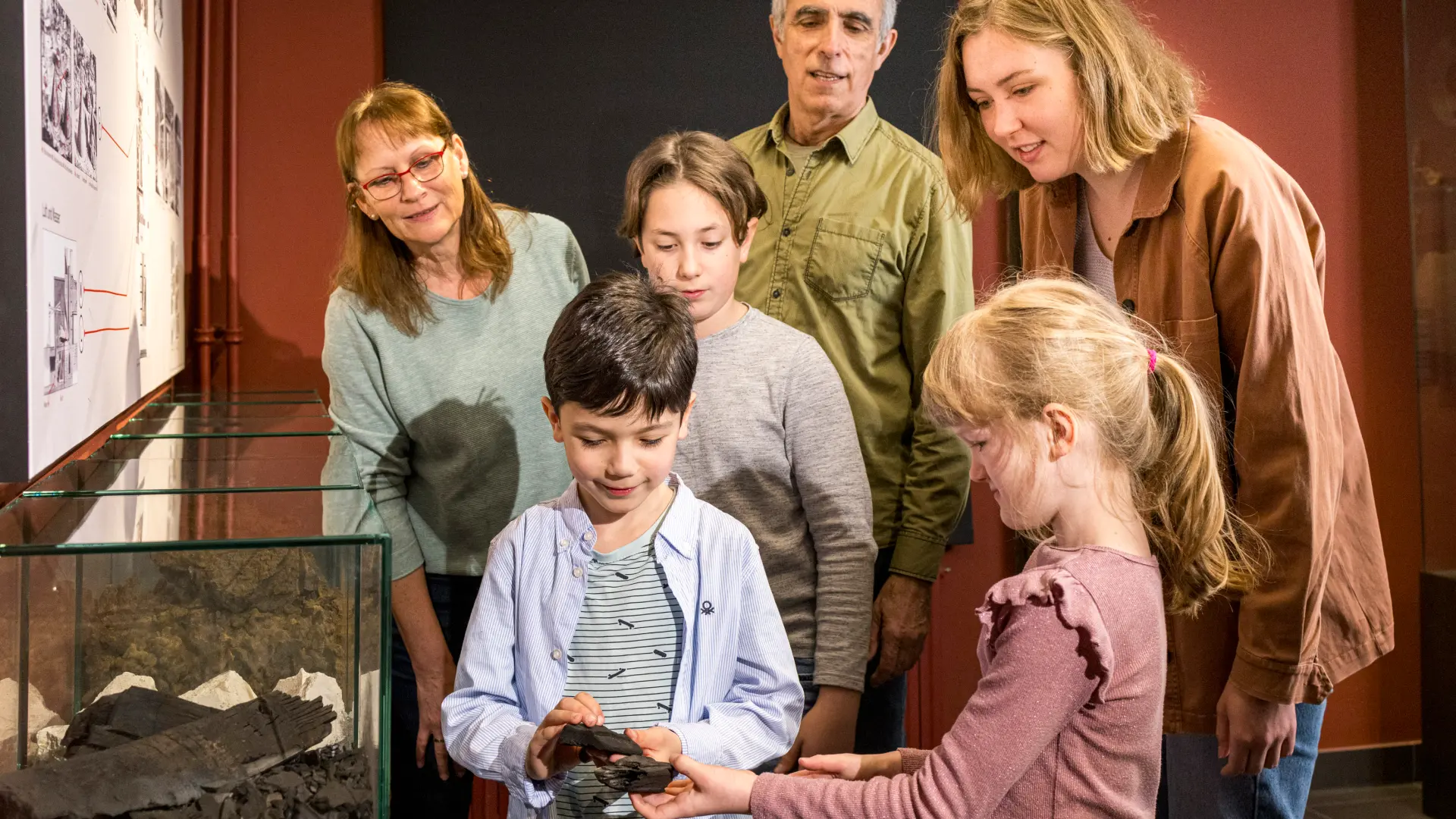 Eine größere Gruppe aus Kindern und Erwachsenen steht neben einer Vitrine und betrachtet Eisenstein.