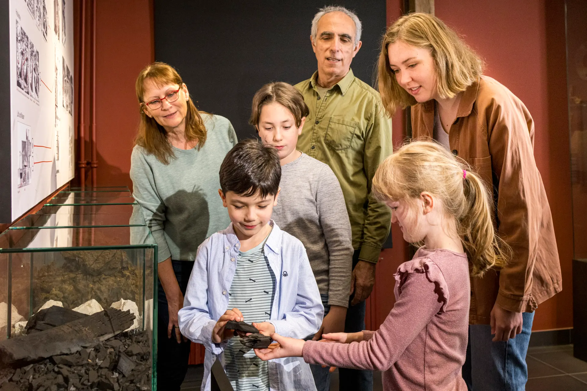 Eine größere Gruppe aus Kindern und Erwachsenen steht neben einer Vitrine und betrachtet Eisenstein.