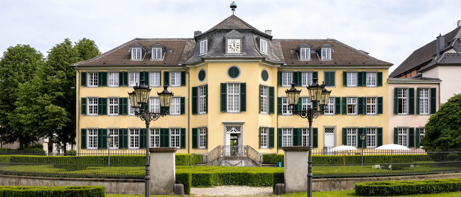 Ein barockes, gelbes Herrenhaus mit vielen Fenstern mit grünen Fensterläden.