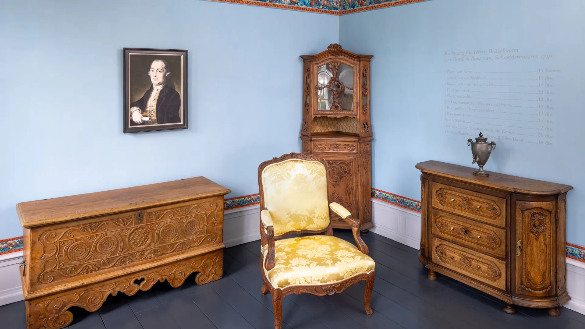 Blick in eine Ausstellung mit historischen Möbeln und Wandportait