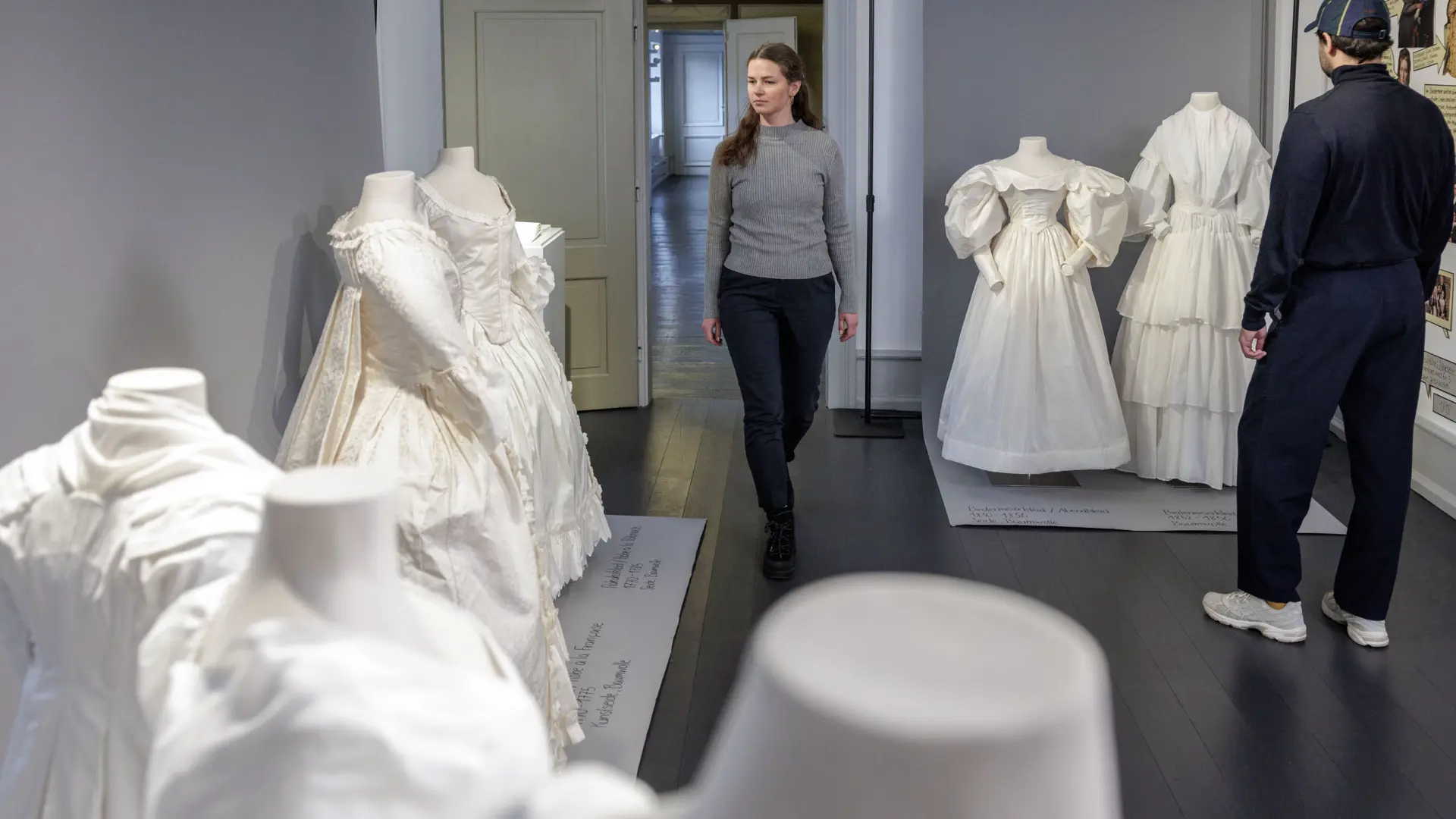 Ein Mann und eine Frau in einem Ausstellungsraum mit weißen Kleidern an Figurinen