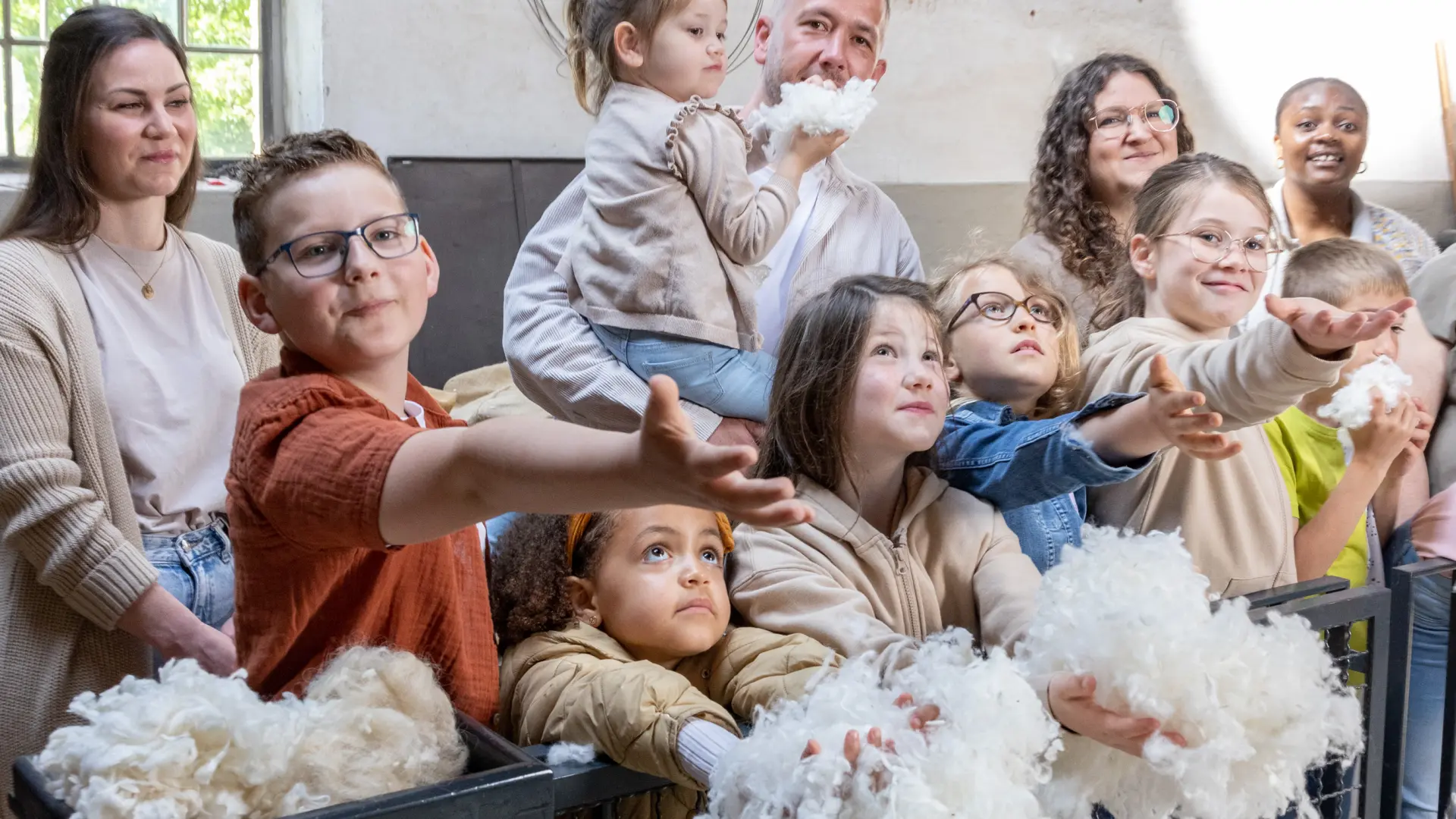 Eine Gruppe von Kindern und Erwachsenen streckt die Hände aus, um Rohwolle zu fangen.