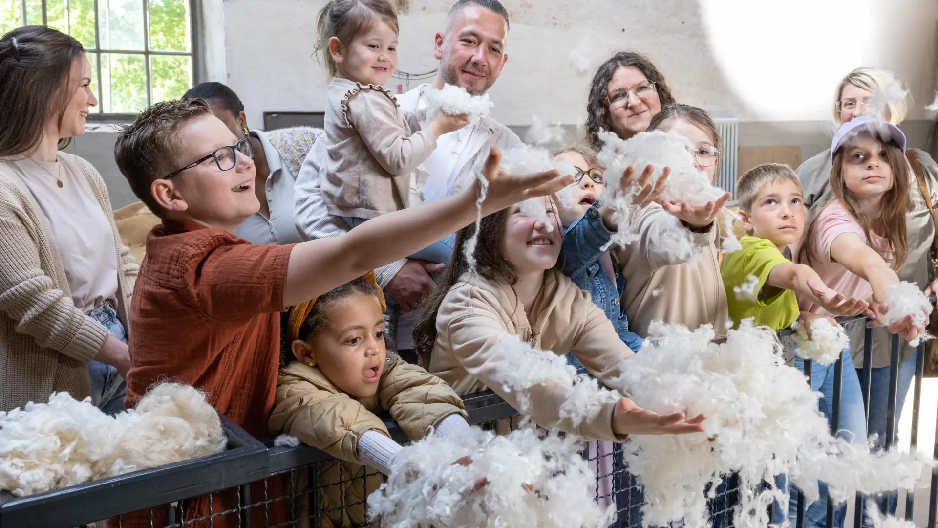 Eine Gruppe aus Erwachsenen und Kindern fängt Rohwolle mit den Händen, die von oben herab rieselt.