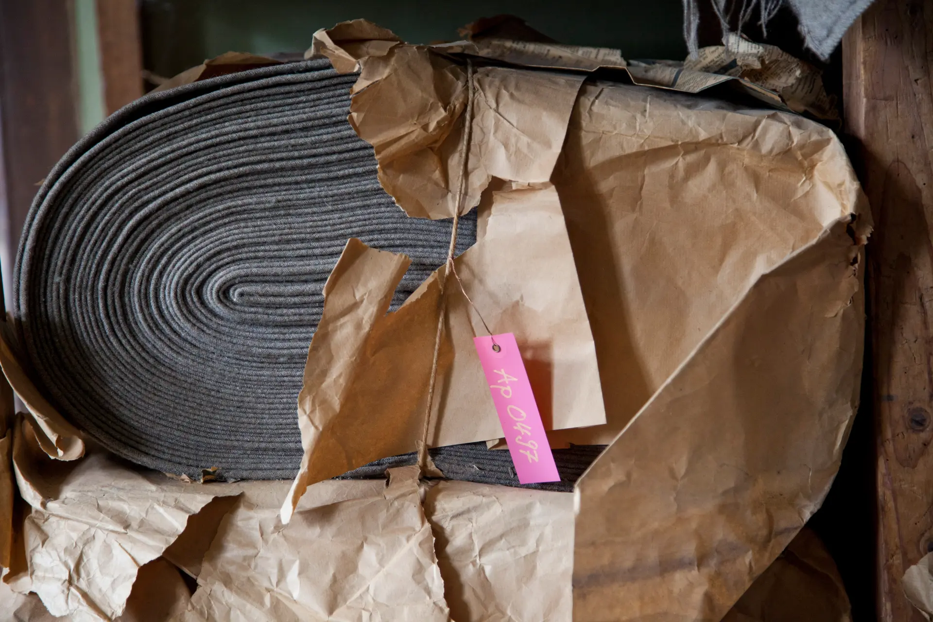 Ein grauer Stoffballen halb verpackt in seitlich aufgerissenem Packpapier.