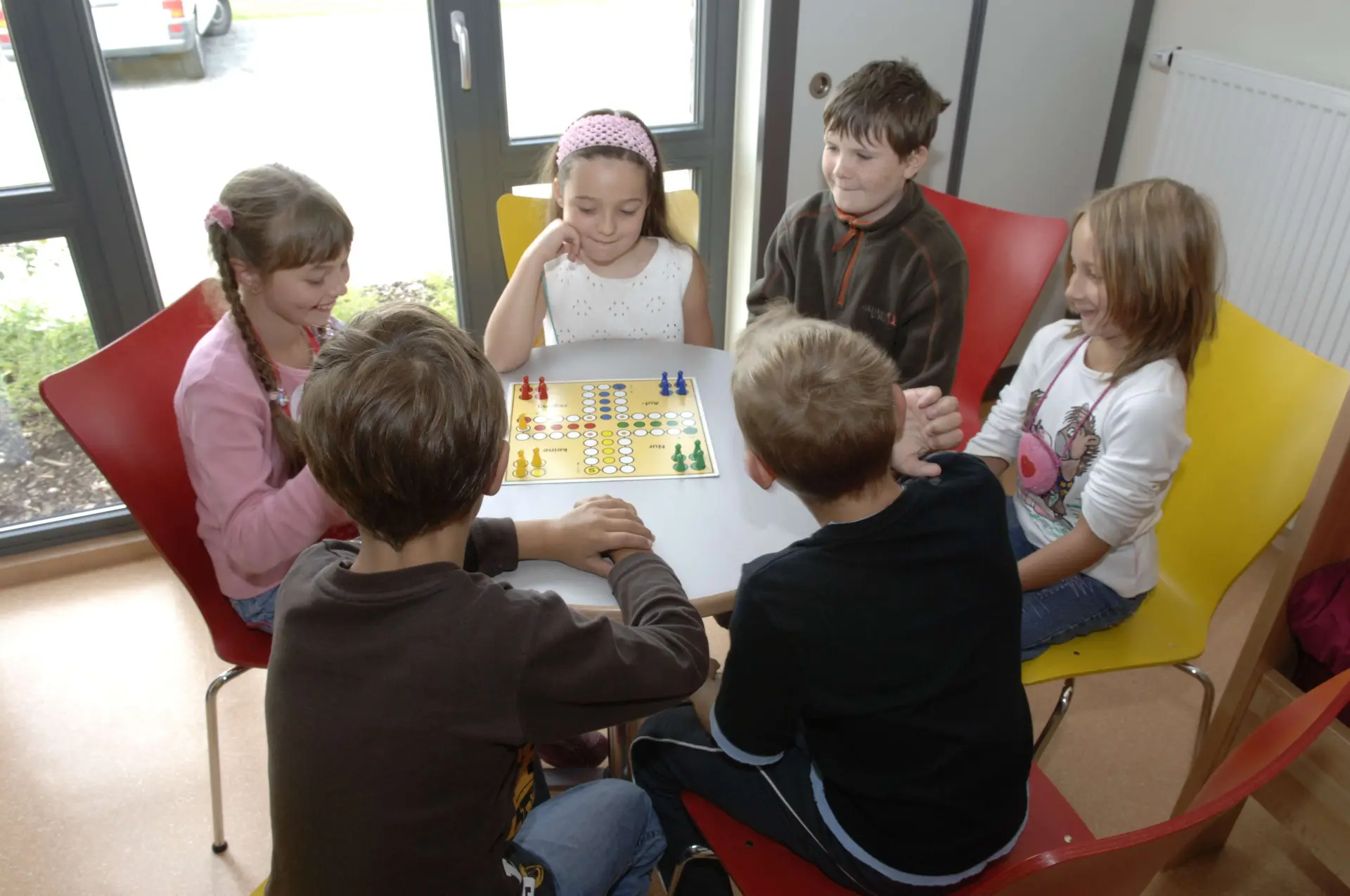 Sechs Kinder spielen Mensch ärger dich nicht an einem Tisch.
