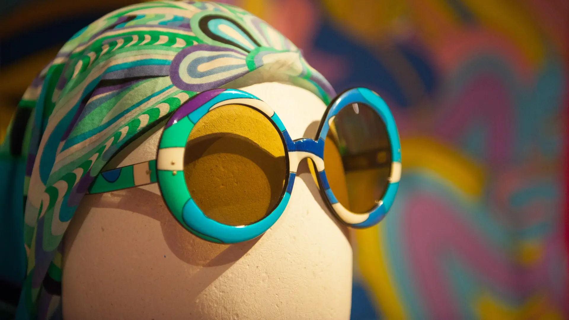 Kopf einer Figurine, die ein gemustertes Kopftuch und eine große Sonnenbrille trägt.