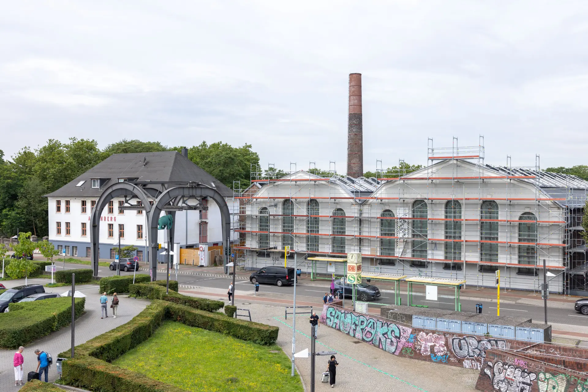 Blick über einen Platz und eine Straße hinaus auf zwei weiße Gebäude. Eines der Gebäude ist von einem Baustellengerüst umgeben.