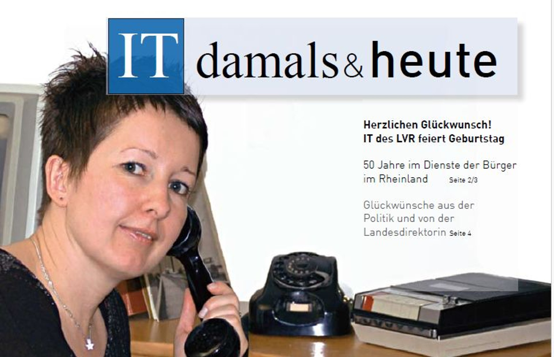 Eine Frau mit einem alten Telefonhörer in der Hand sitzt an einem Tisch und lächelt in die Kamera.