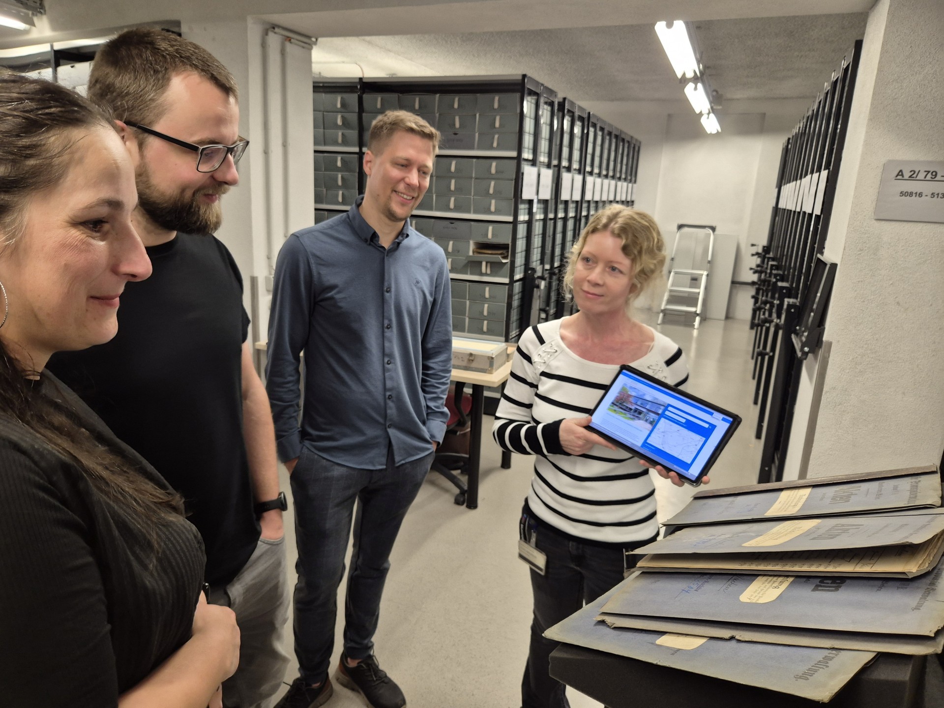Eine Frau zeigt drei Personen im LVR-Archiv auf einem Tablet das digitale Portal Archive NRW.