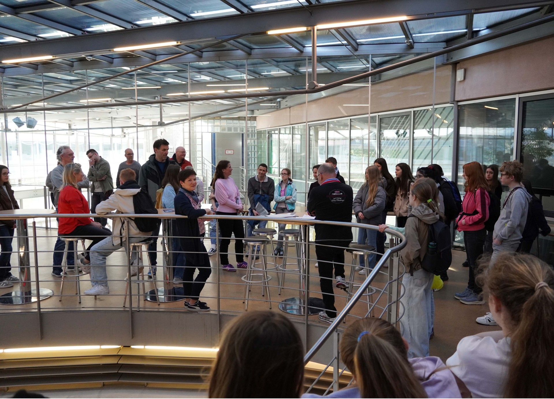 Eine Frau spricht zu zahlreichen Personen in einem Foyer.