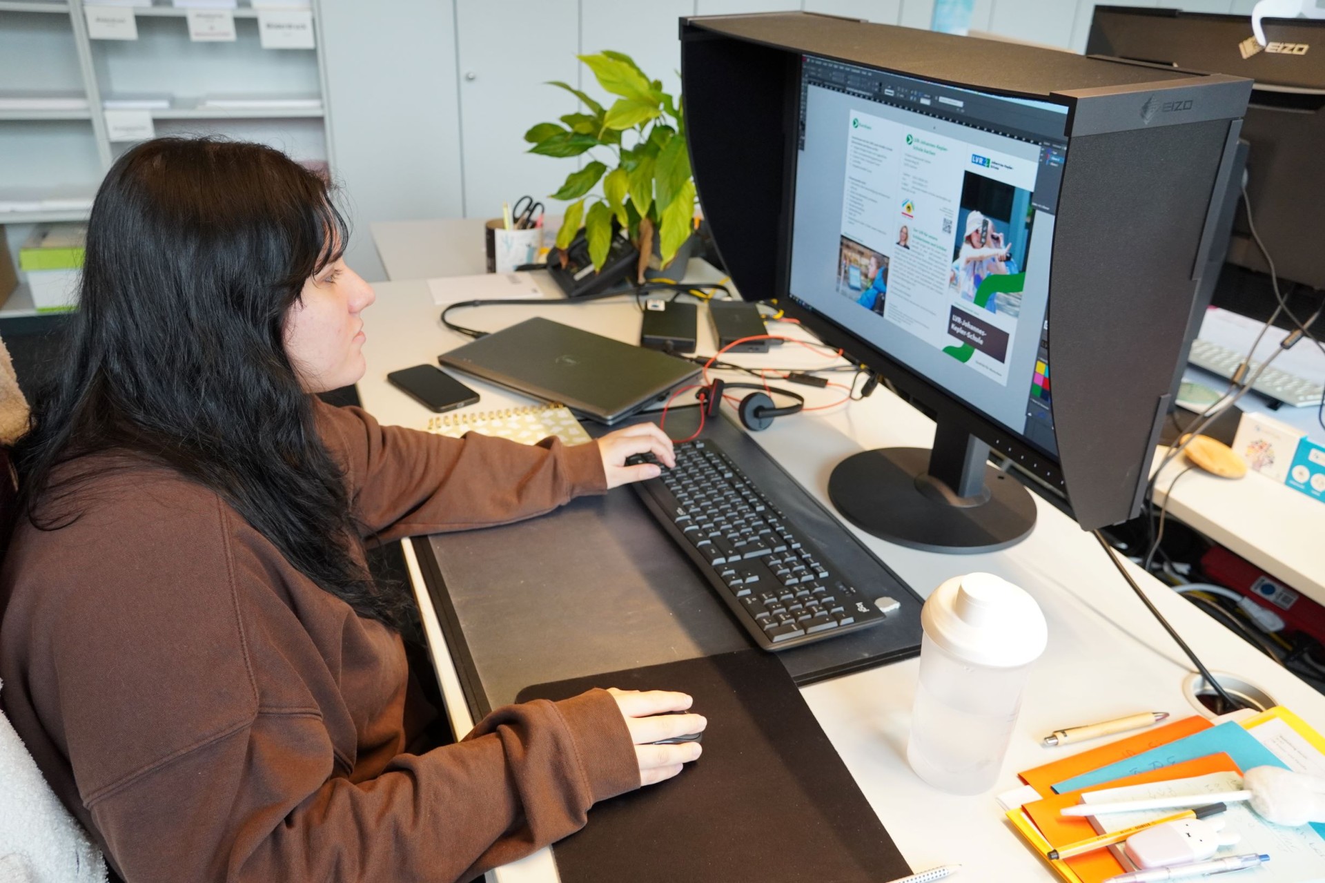 Eine Frau sitzt vor einem Monitor, auf dem ein Flyer zu sehen ist.