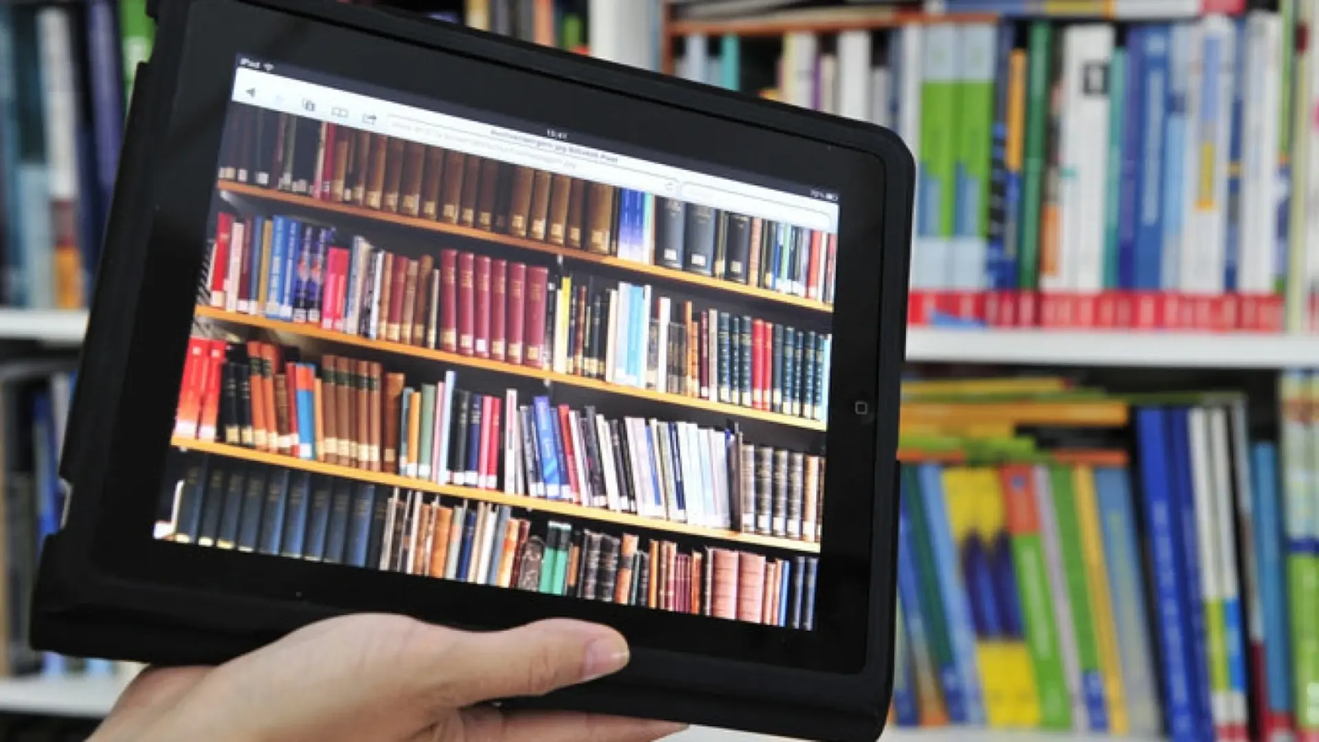 Ein Tablet mit dem Bild eines Bücherregals wird vor ein reales Bücherregal gehalten.