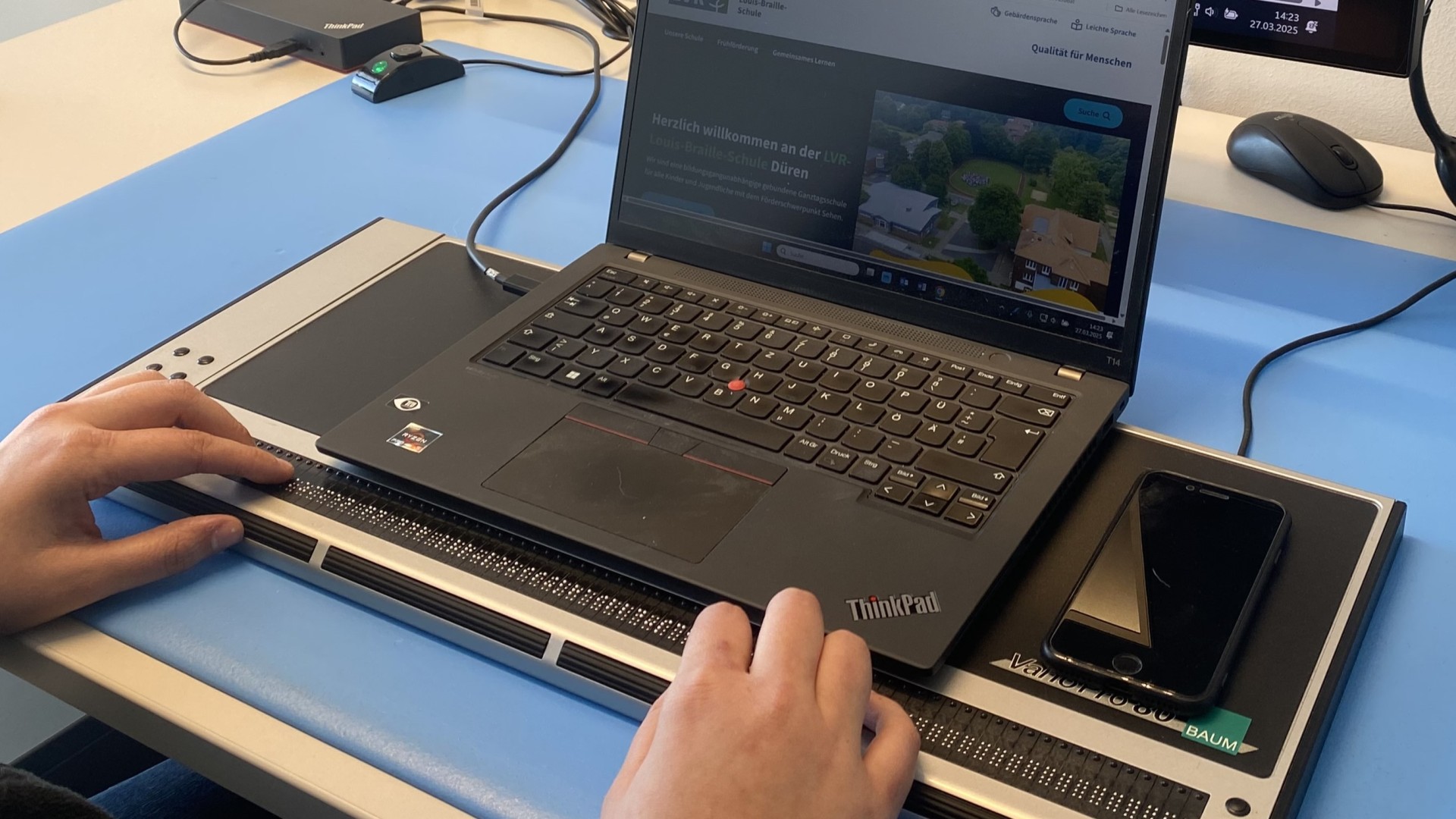 Zwei Hände an einer Braille-Tastatur bedienen ein Laptop.