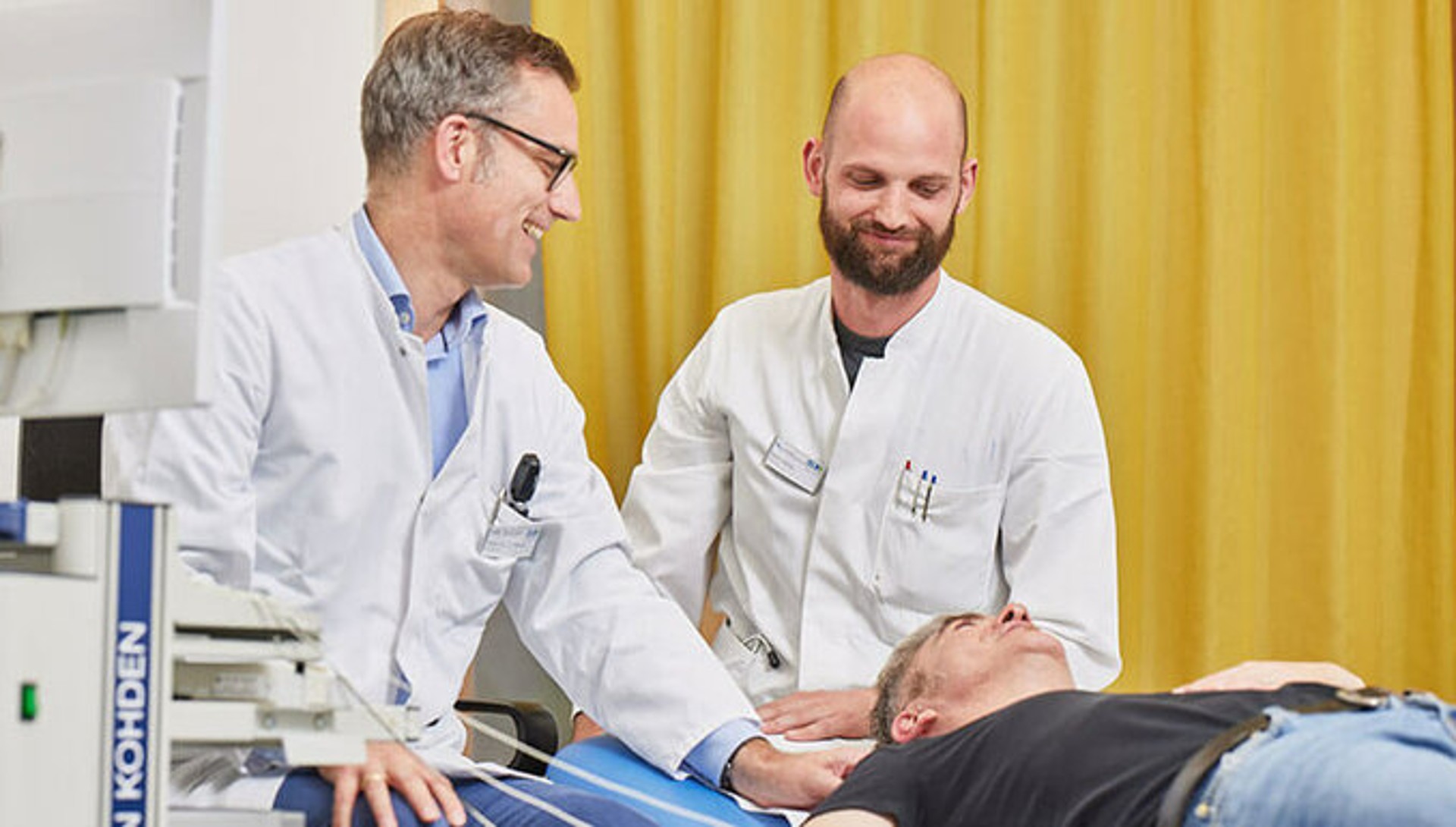 Zwei Ärzte sitzen hinter einem liegenden Patienten