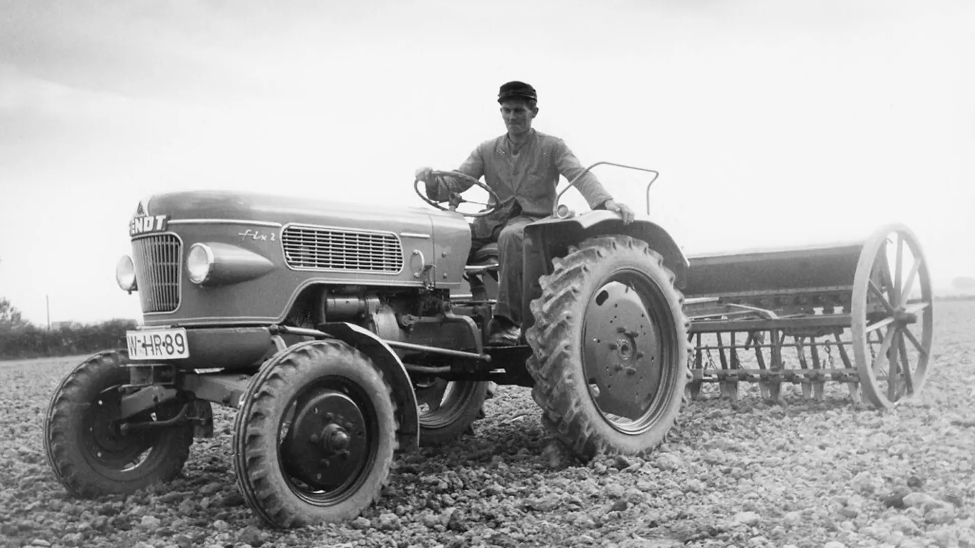 Traktor mit angehängten Pflug, gesteuert von einer männlichen Person