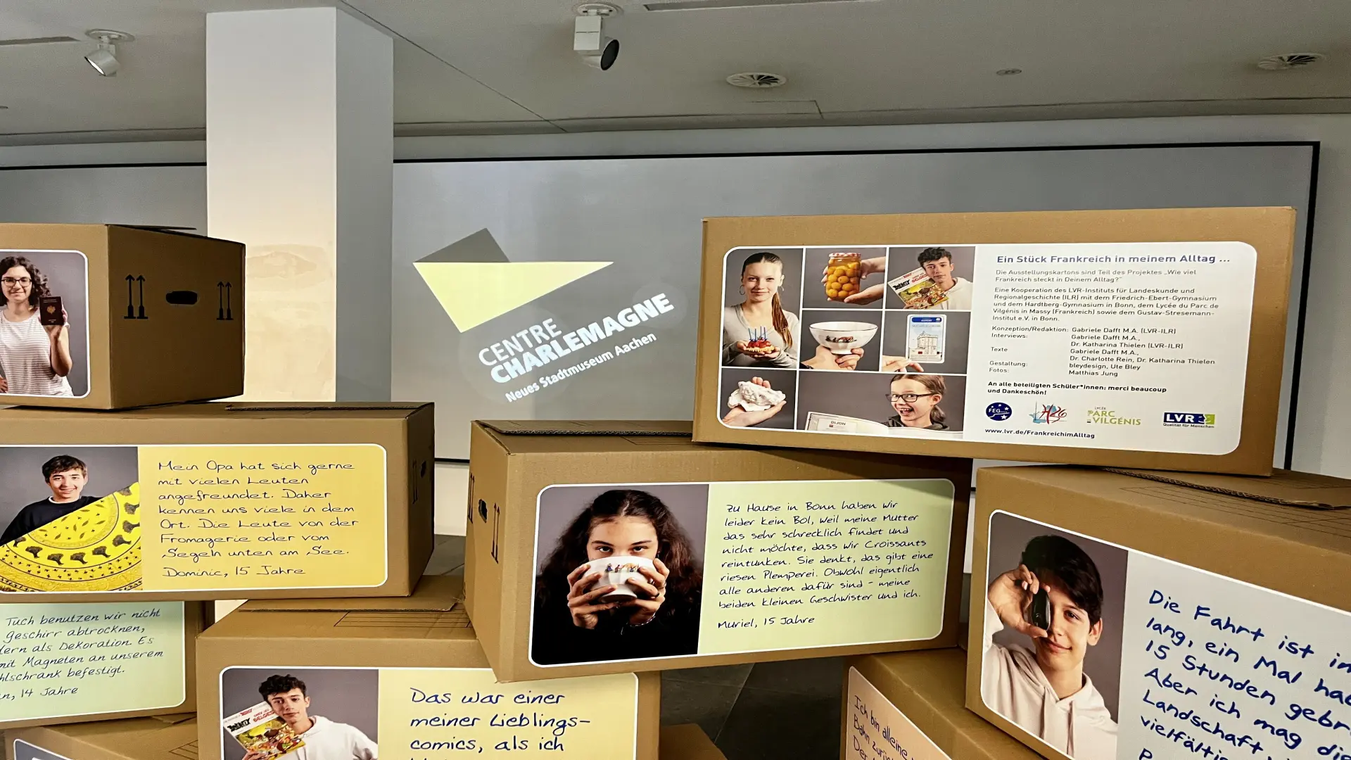 Kartons gestappelt. Auf den kartons sind Fotos und Zitate von Schüler*innen abgebildet.