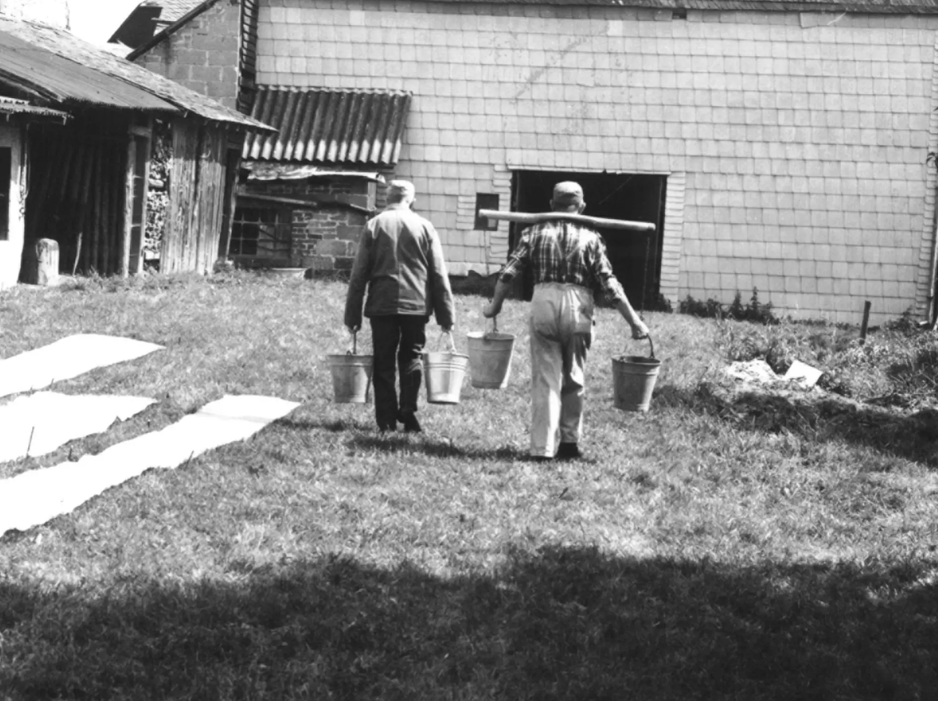 Zwei Männer laufen während der Dreharbeiten für den Film "Bäuerliche Leinenweberei" mit Eimern in den Händen zwischen den Tuchbahnen entlang.