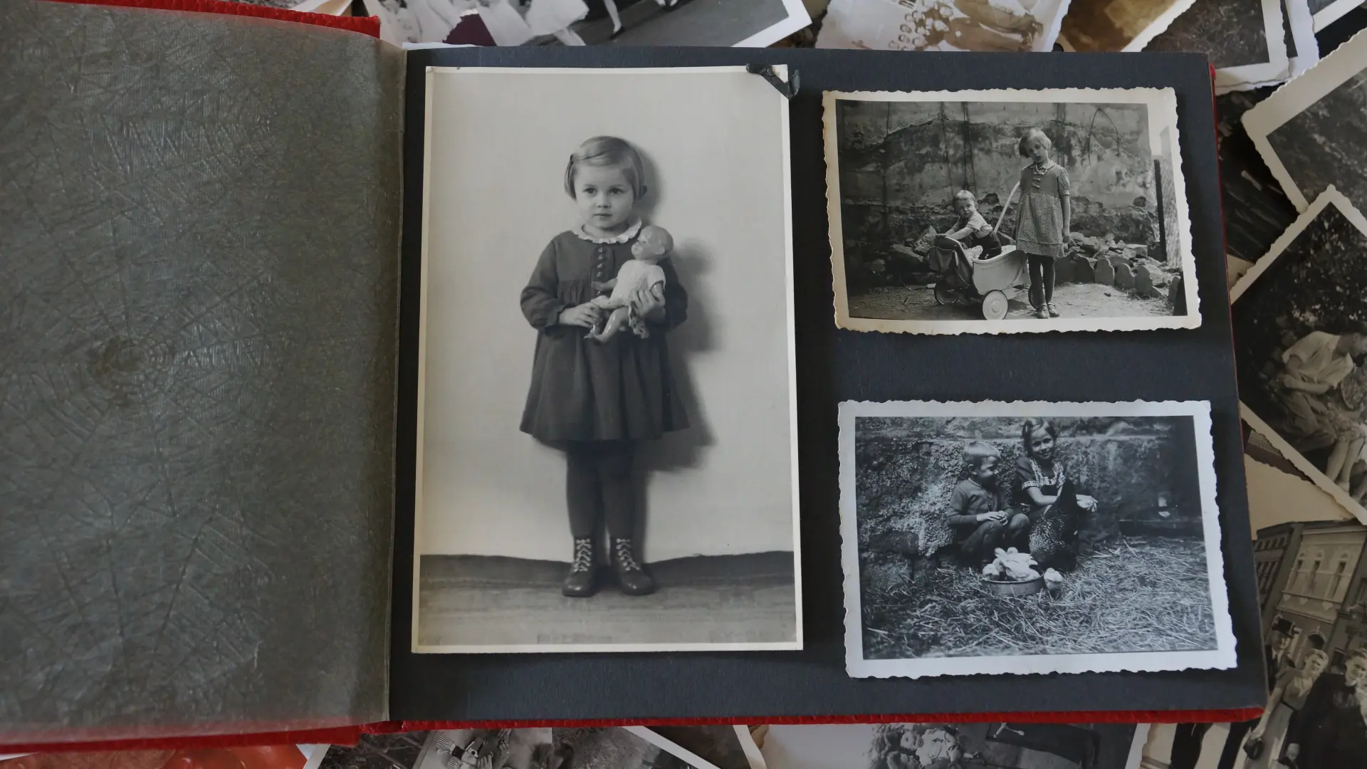 Aufgeschlagenes Fotoalbumseite mit drei Bildern, links Mädchen mit Puppe im Arm