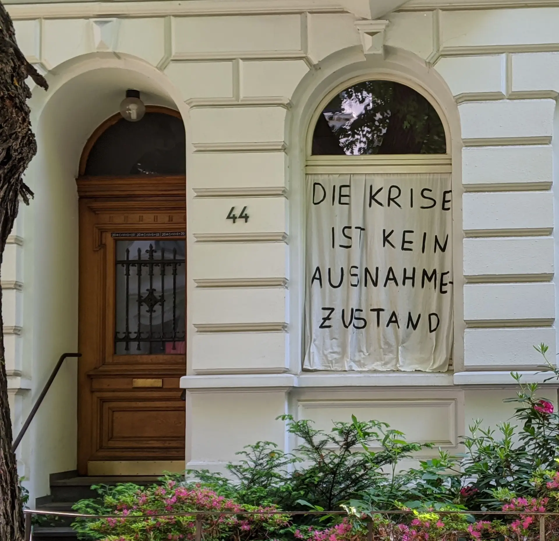 Hausansicht: Im Fenster hängt ein Bettlaken mit der Aufschrift " Die Krise ist kein Ausnahmezustand.