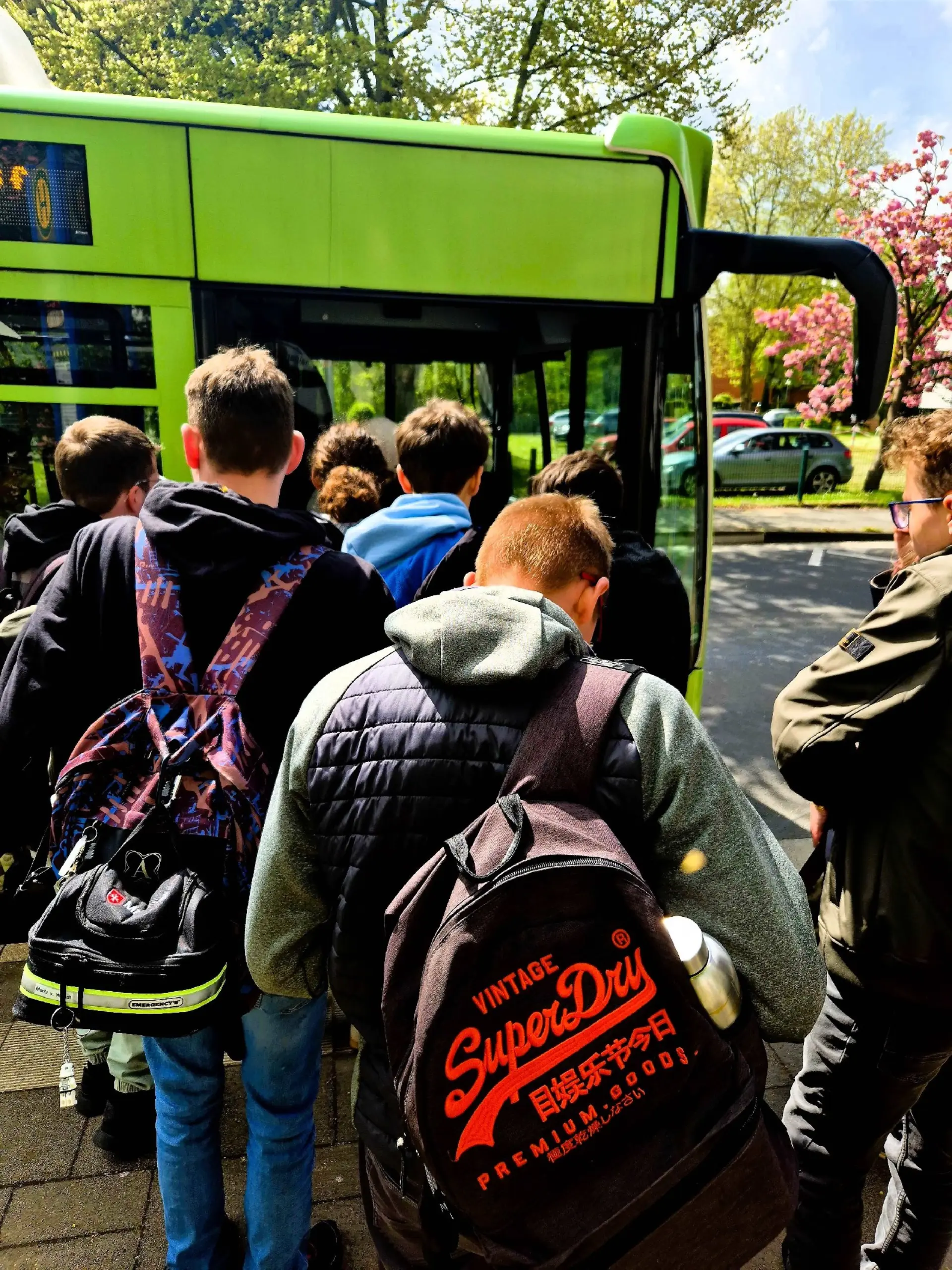Schüler*innen warten vor einem Bus auf den Einstieg