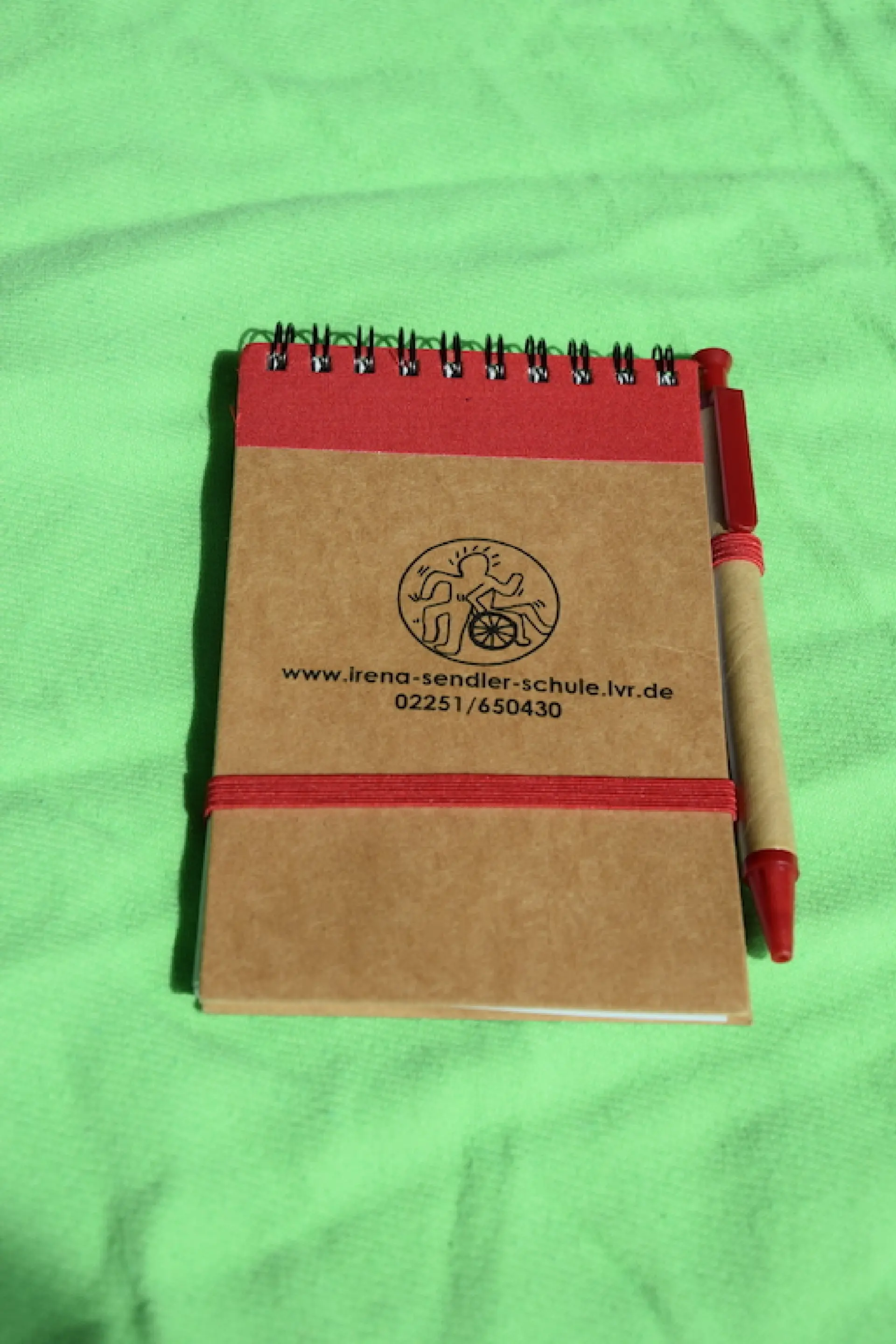 Produkt aus dem Shop des Fördervereins: brauner Notizblock mit Schullogo