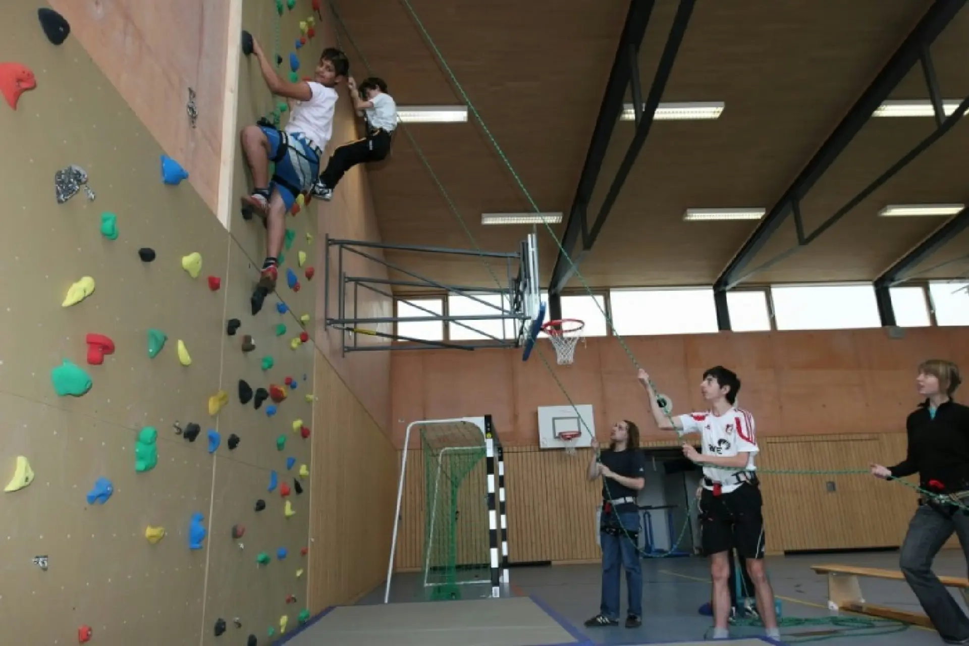 Kinder klettern in der Turnhalle an einer Kletterwand