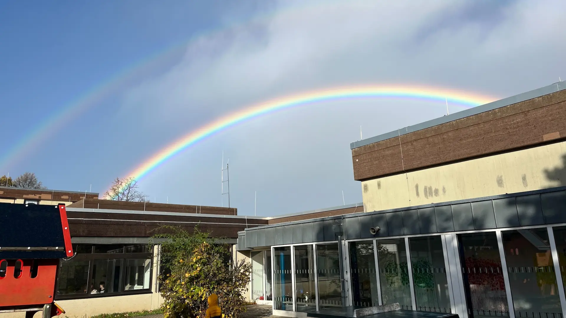 Blick auf das Schulgebäude, am Himmel prangt ein bunter Regenbogen