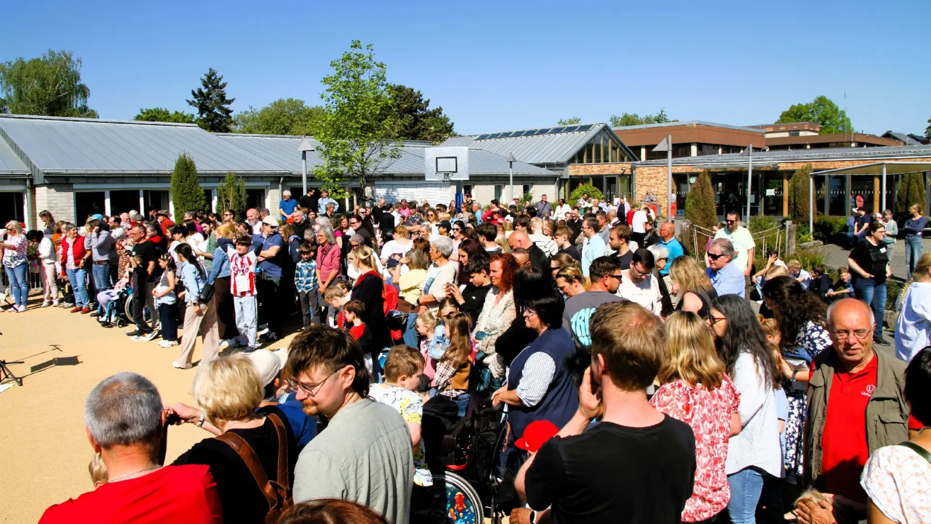 Zahlreiche Besucher*innen des Schulfests stehen auf dem Schulhof