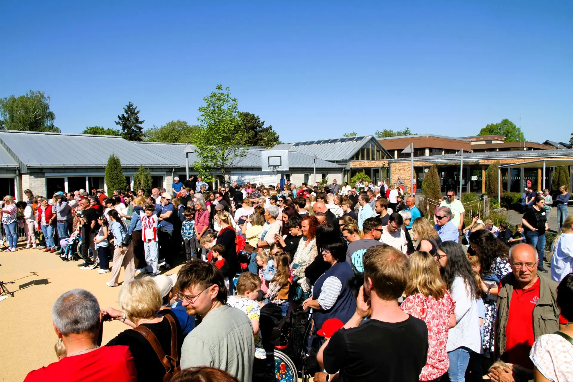 Zahlreiche Besucher*innen des Schulfests stehen auf dem Schulhof