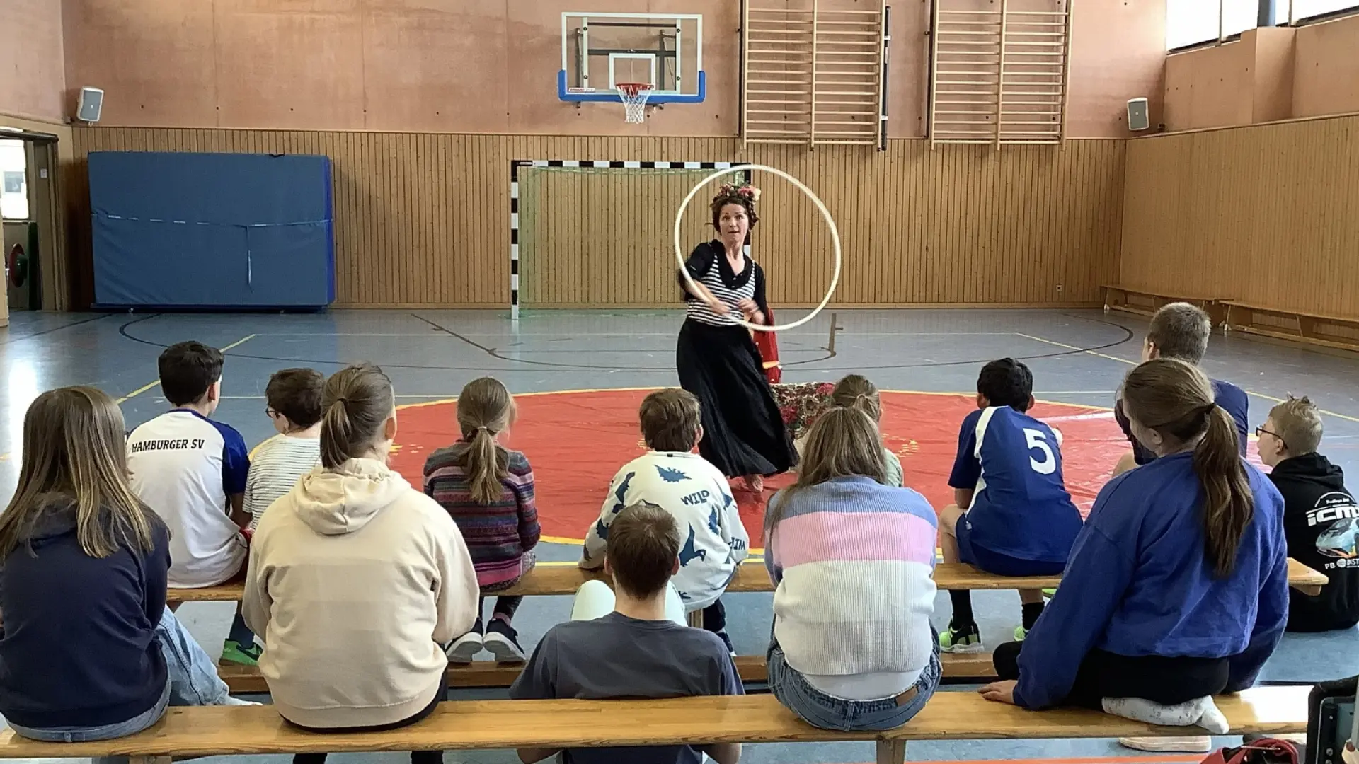 Kinder sitzen in Turnhalle und schauen Artistin zu