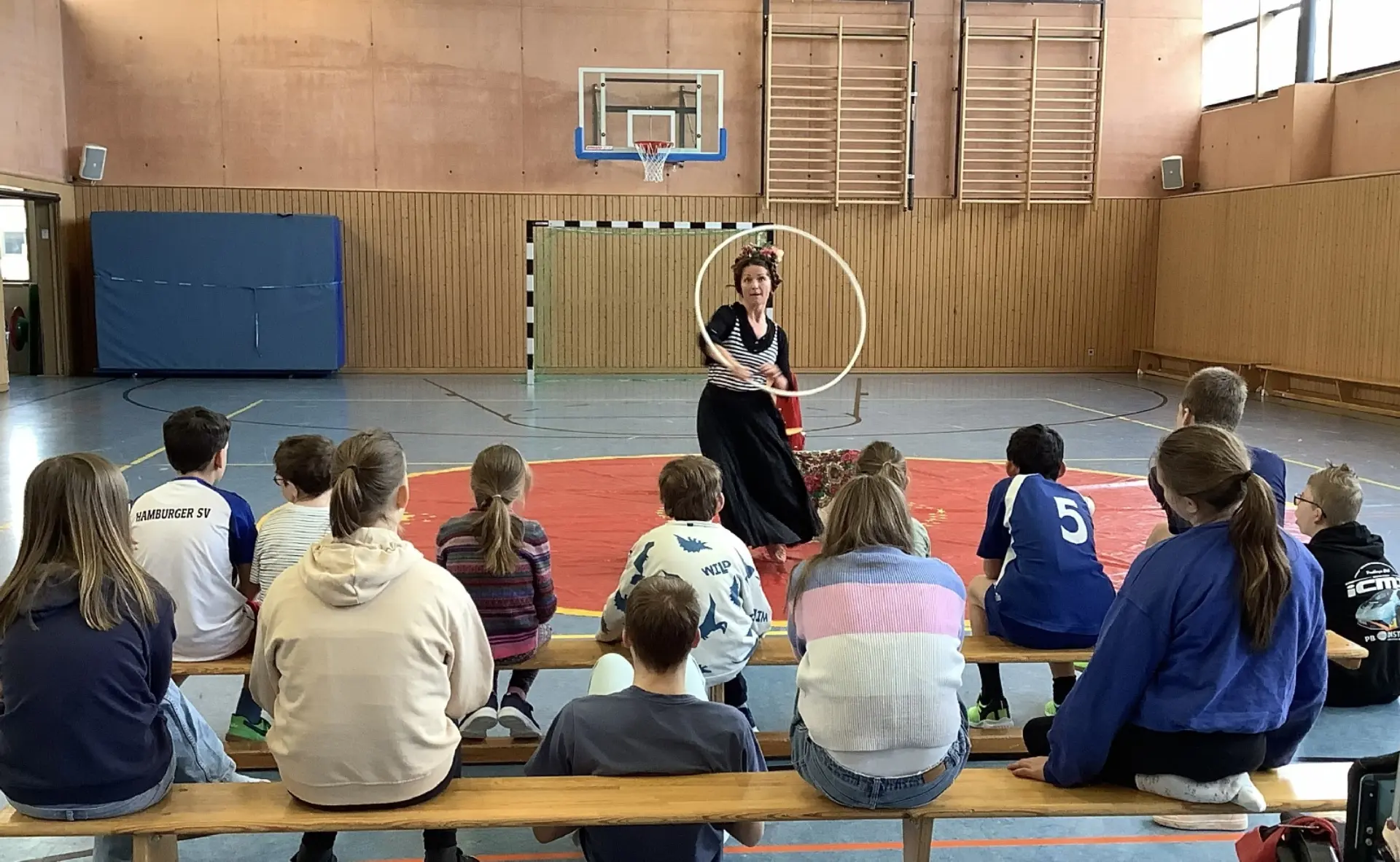 Kinder sitzen in Turnhalle und schauen Artistin zu