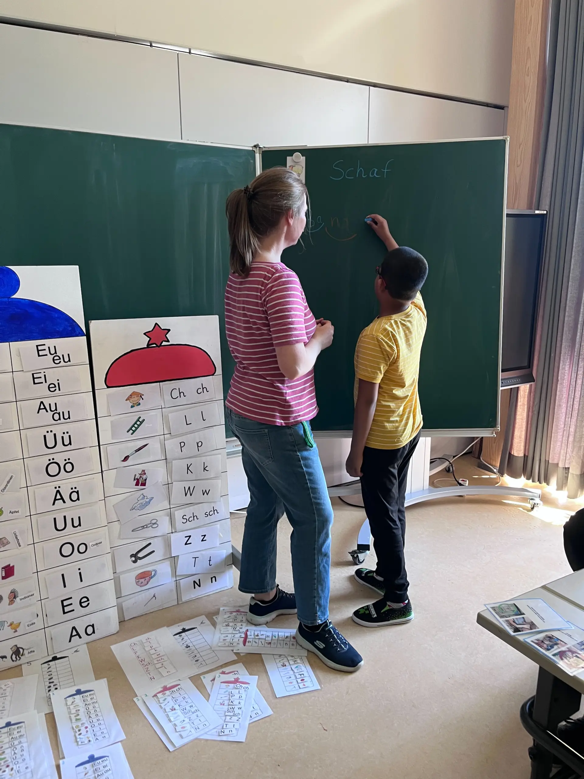 Unterricht in der Primarstufe: ein Kind schreibt "Schaf" an die Tafel