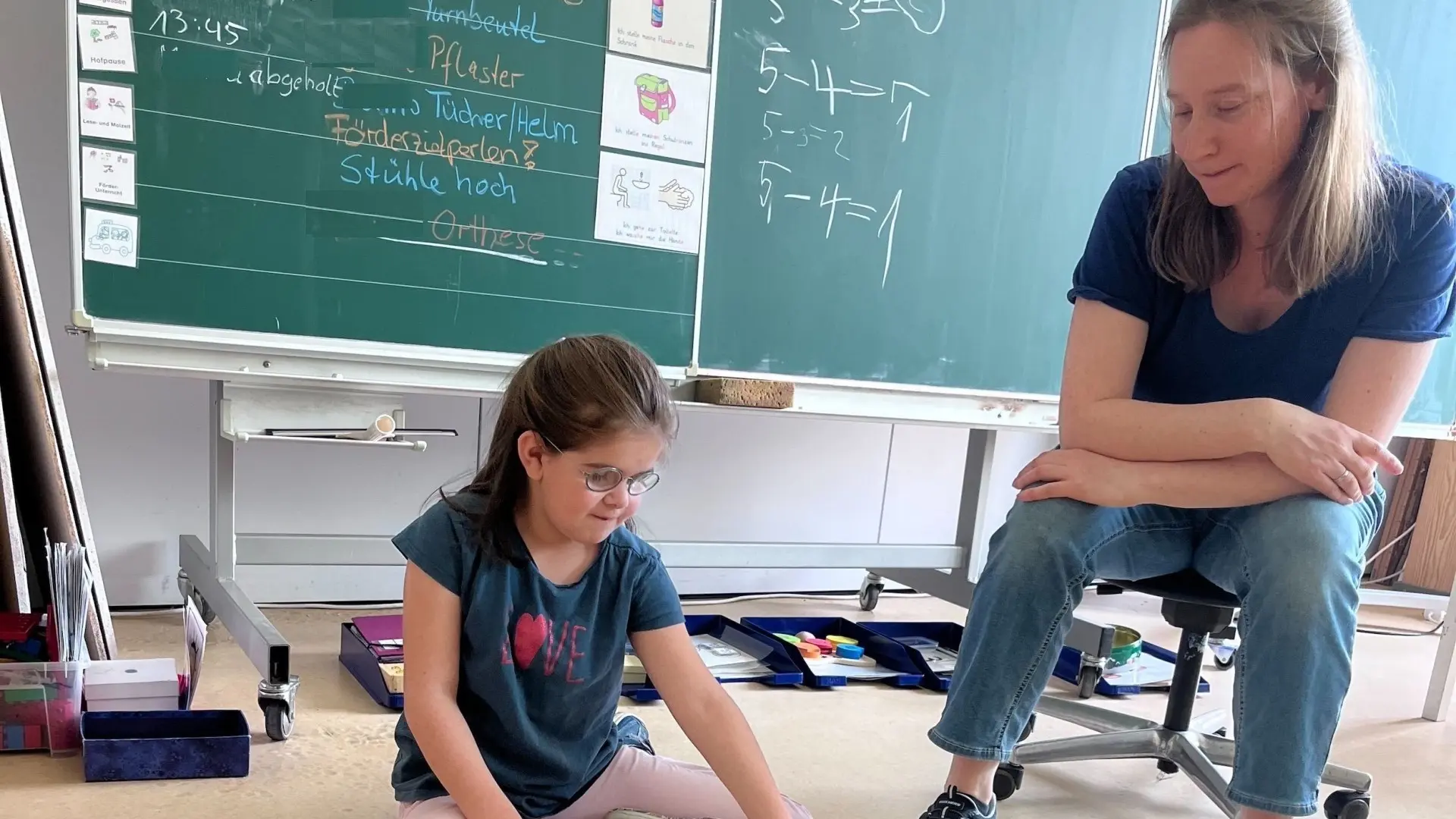 Primarstufe: Kind sitzt vor der Tafel auf dem Boden und zählt im Matheunterricht Spielzeugtiere