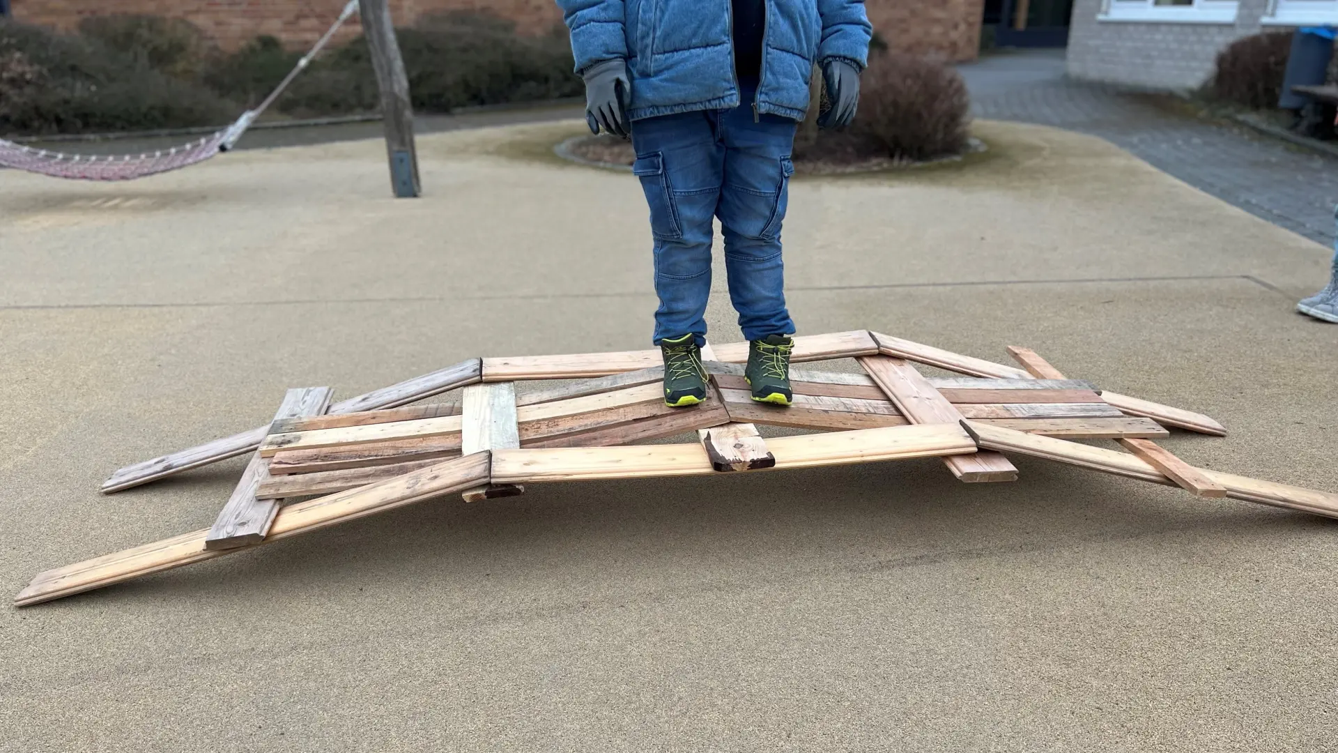 Kind steht auf dem Schulhof auf einer selbstgebauten Holzbrücke